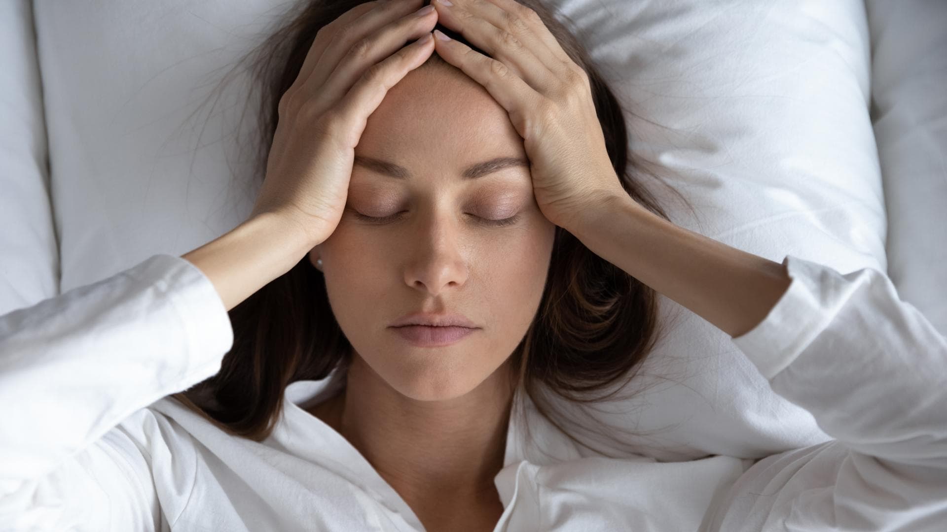 Frau liegt im Bett und hält sich den Kopf