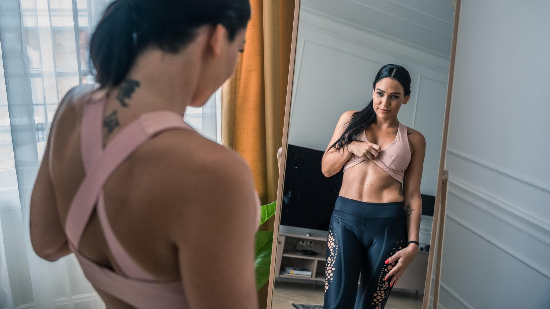 Frau steht vor Spiegel und betrachtet ihren Bauch