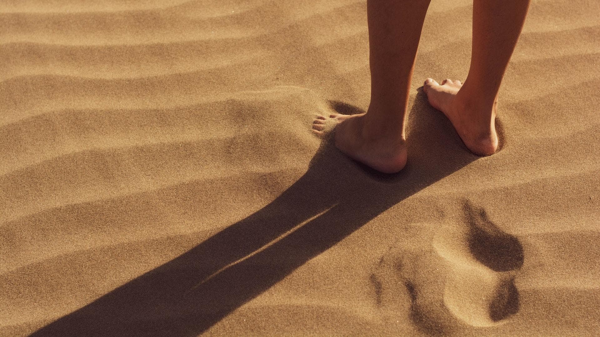 Frau steht barfuß im Sand