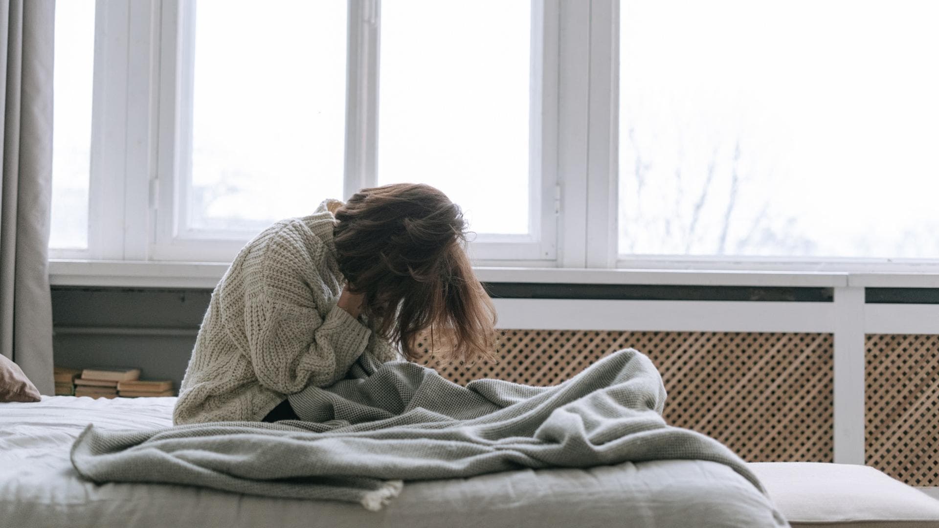 Frau sitzt im Bett und vergräbt ihr Gesicht in ihren Händen Frau sitzt im Bett und vergräbt ihr Gesicht in ihren Händen