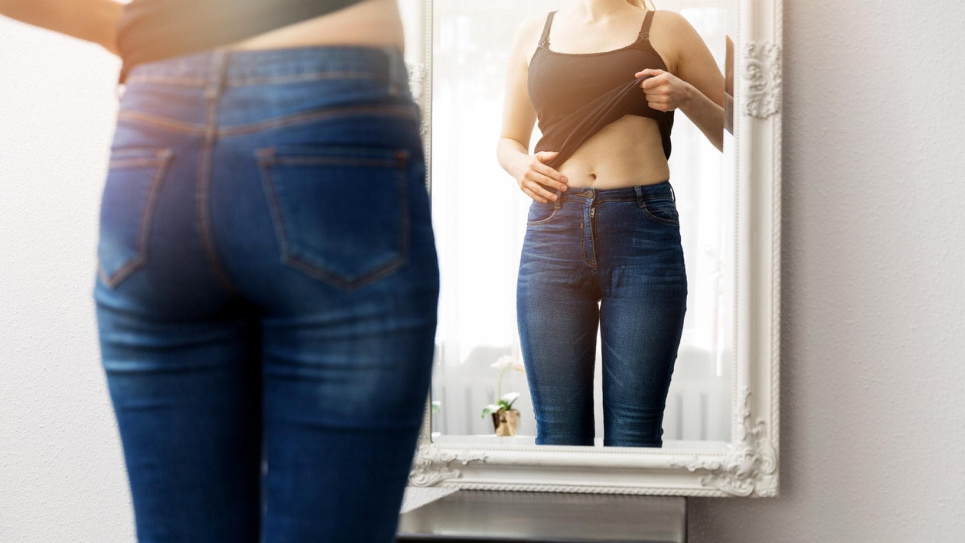 Frau betrachtet ihren Bauch im Spiegel