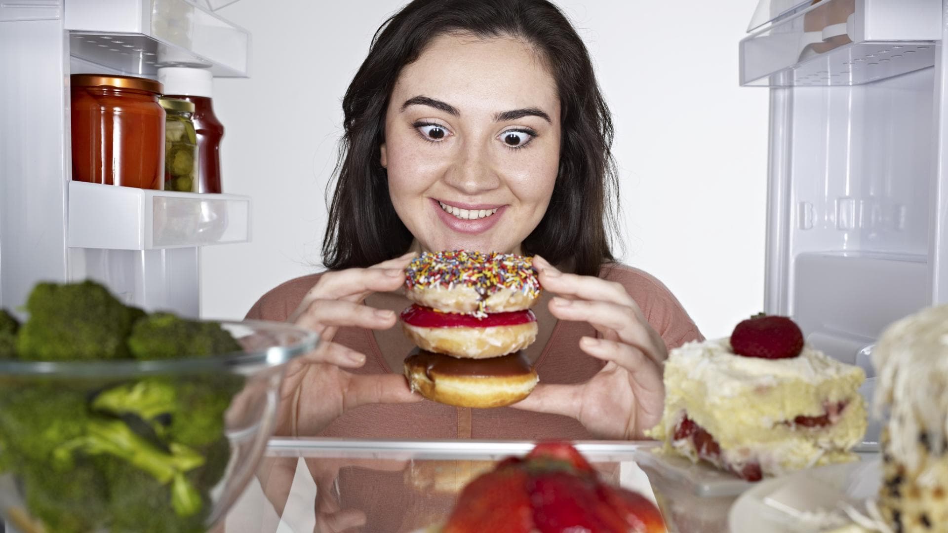 Frau holt drei Donuts aus dem Kühlschrank