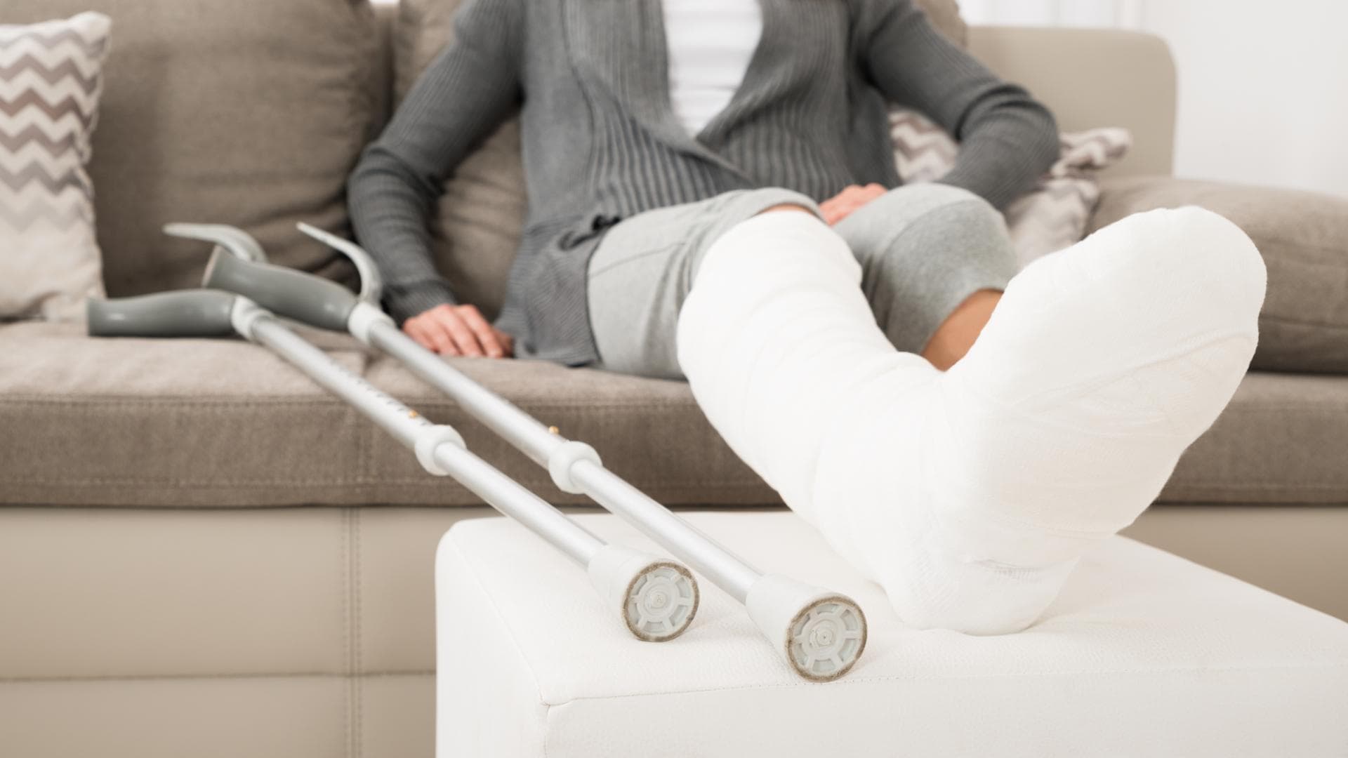 Frau mit Gips und Krücken sitzt auf dem Sofa