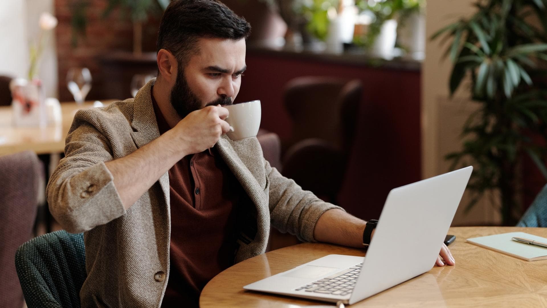 Mann sitzt vor einem Laptop und trinkt Kaffee