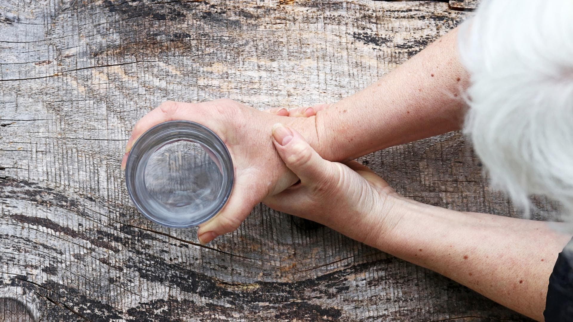 Frau mit grauen Haaren hält Wasserglas in den Händen