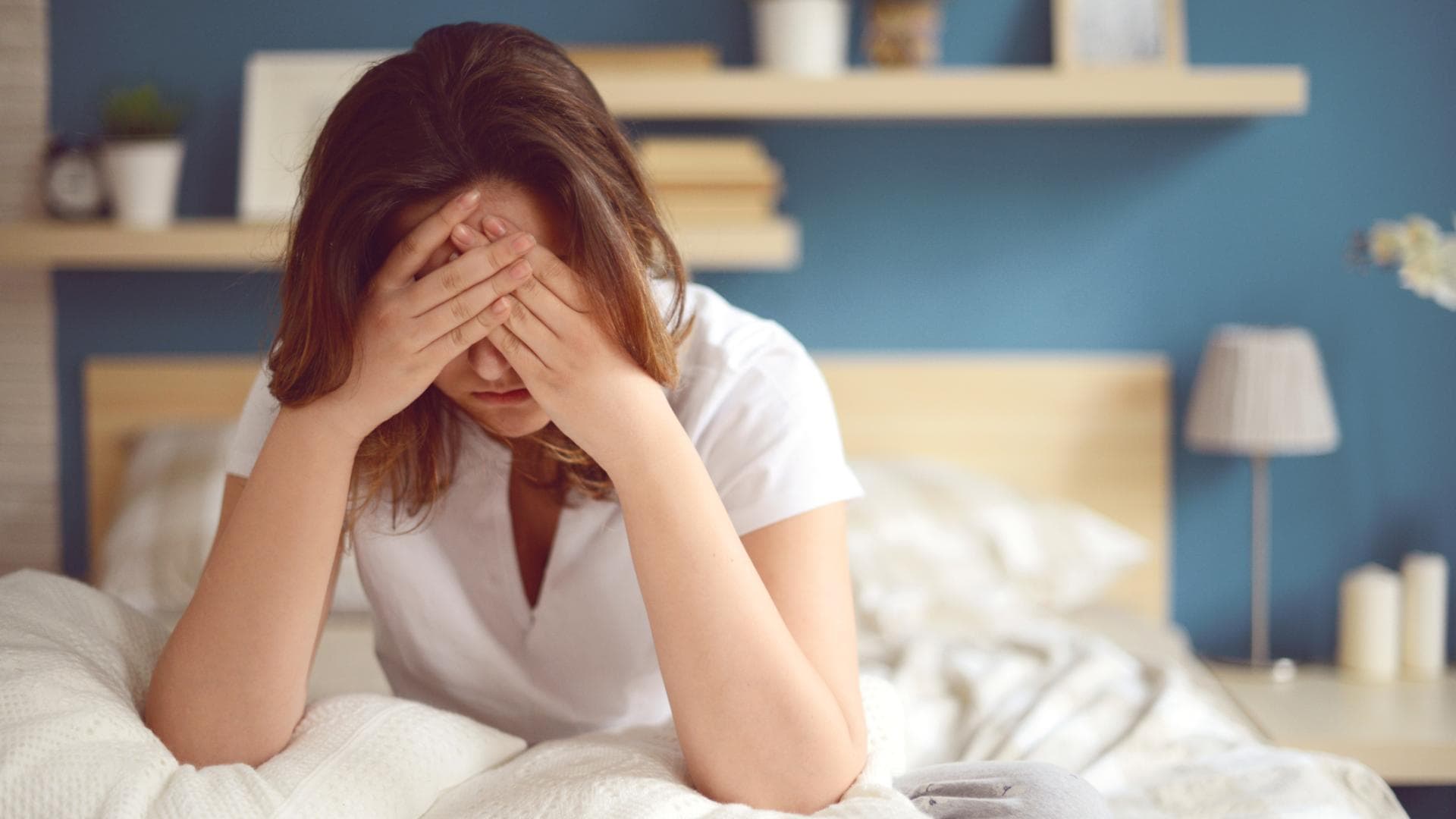 Frau mit Erschöpfung sitzt im Bett mit Händen vor dem Gesicht