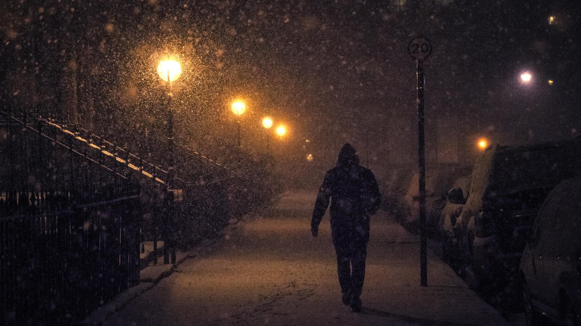 Person geht bei Schneefall am Abend durch dunkle von Laternen beleuchtete Straße