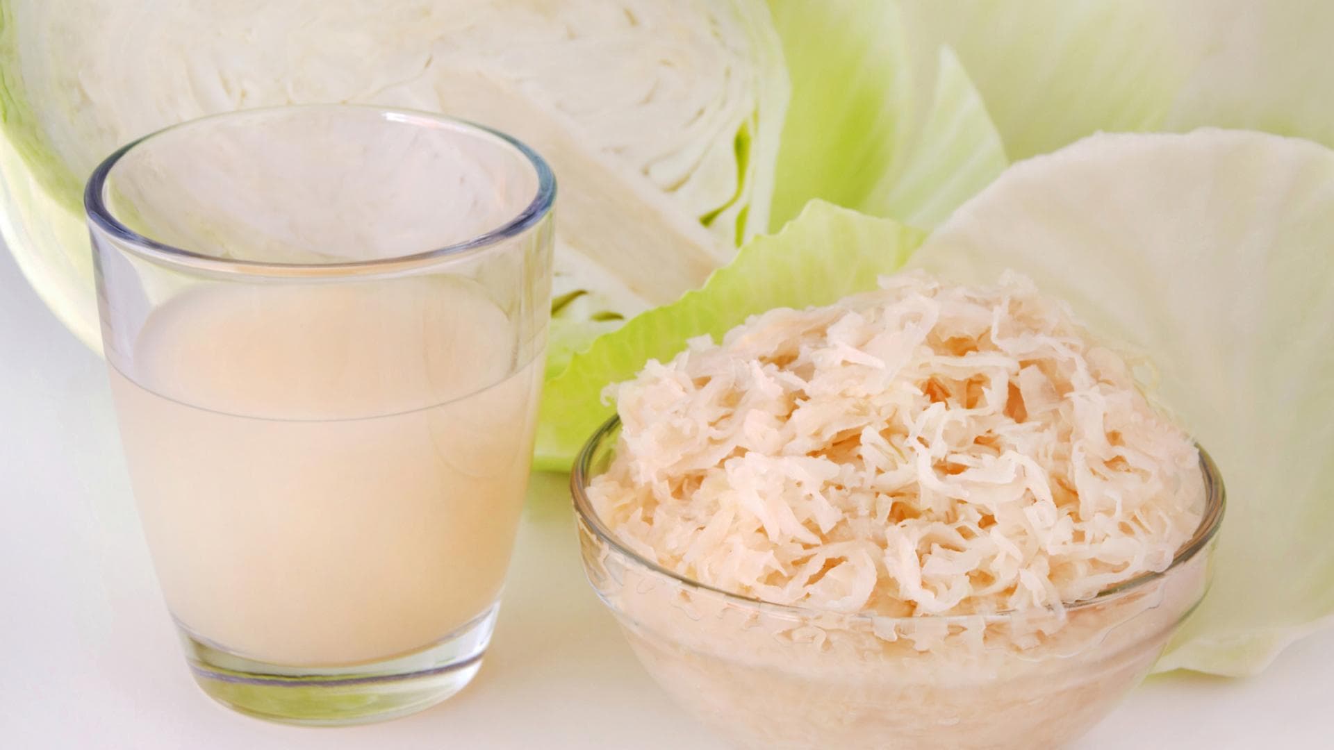 Sauerkraut und Sauerkrautsaft vor aufgeschnittenem Weißkohl