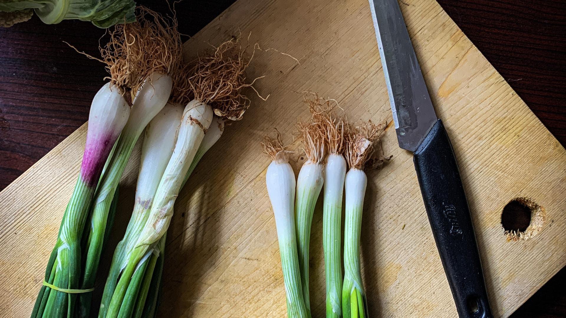 Frühlingszwiebeln auf einem Brett neben einem Messer