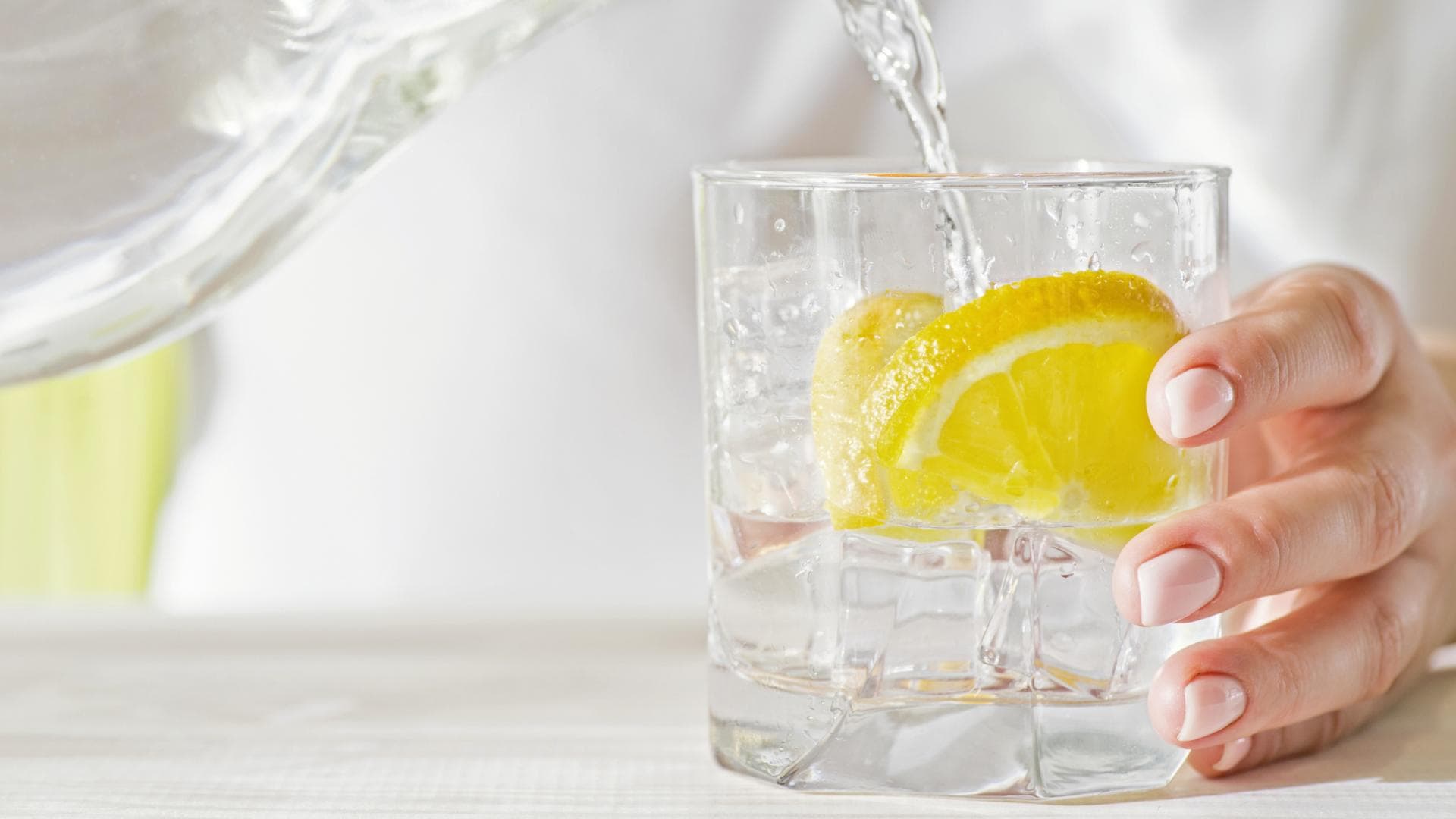 Wasser wird in ein Glas mit Zitrone gegossen