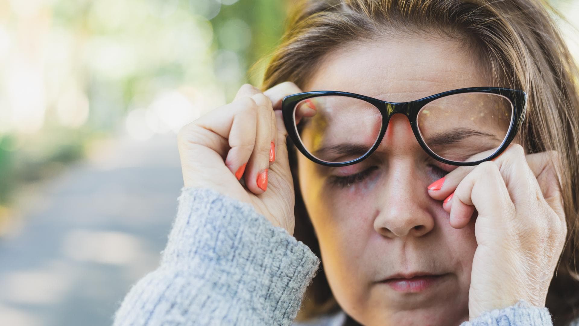 Frau reibt sich das Auge im Freien