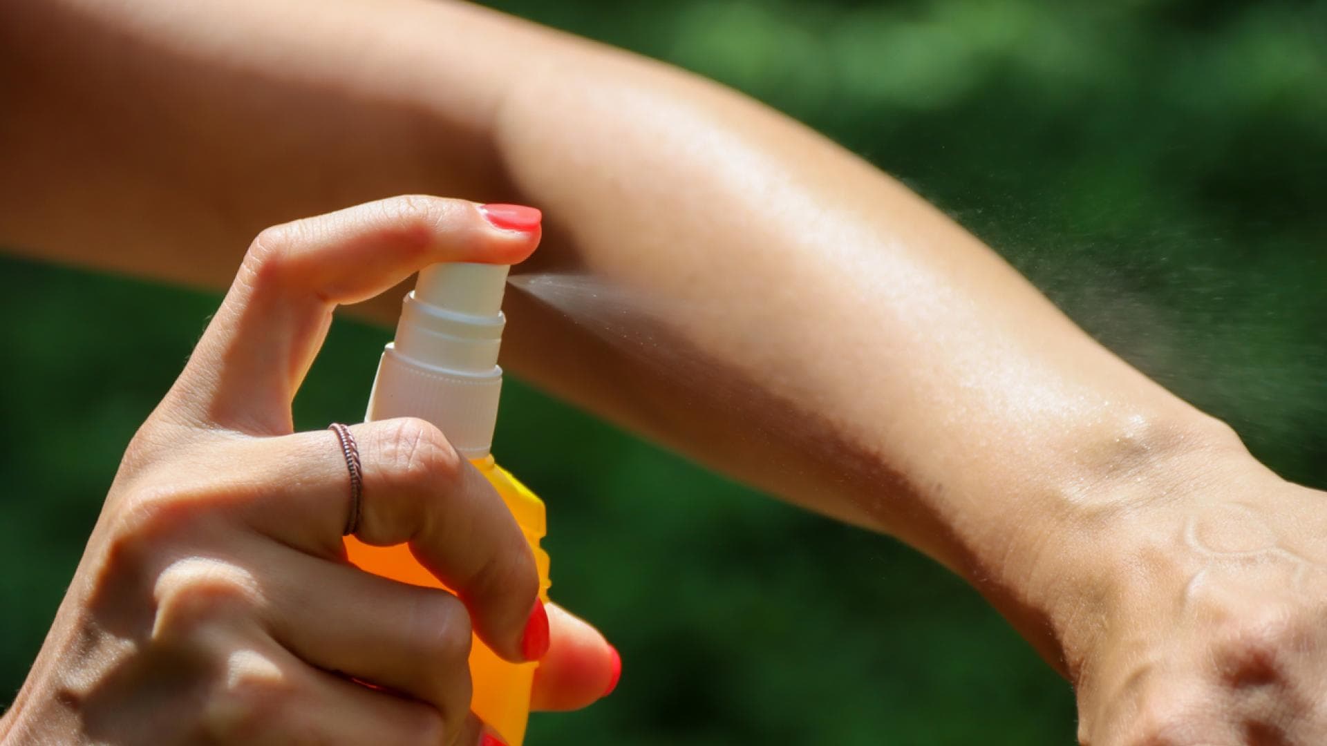 Mensch sprüht Mückenschutzspray auf
