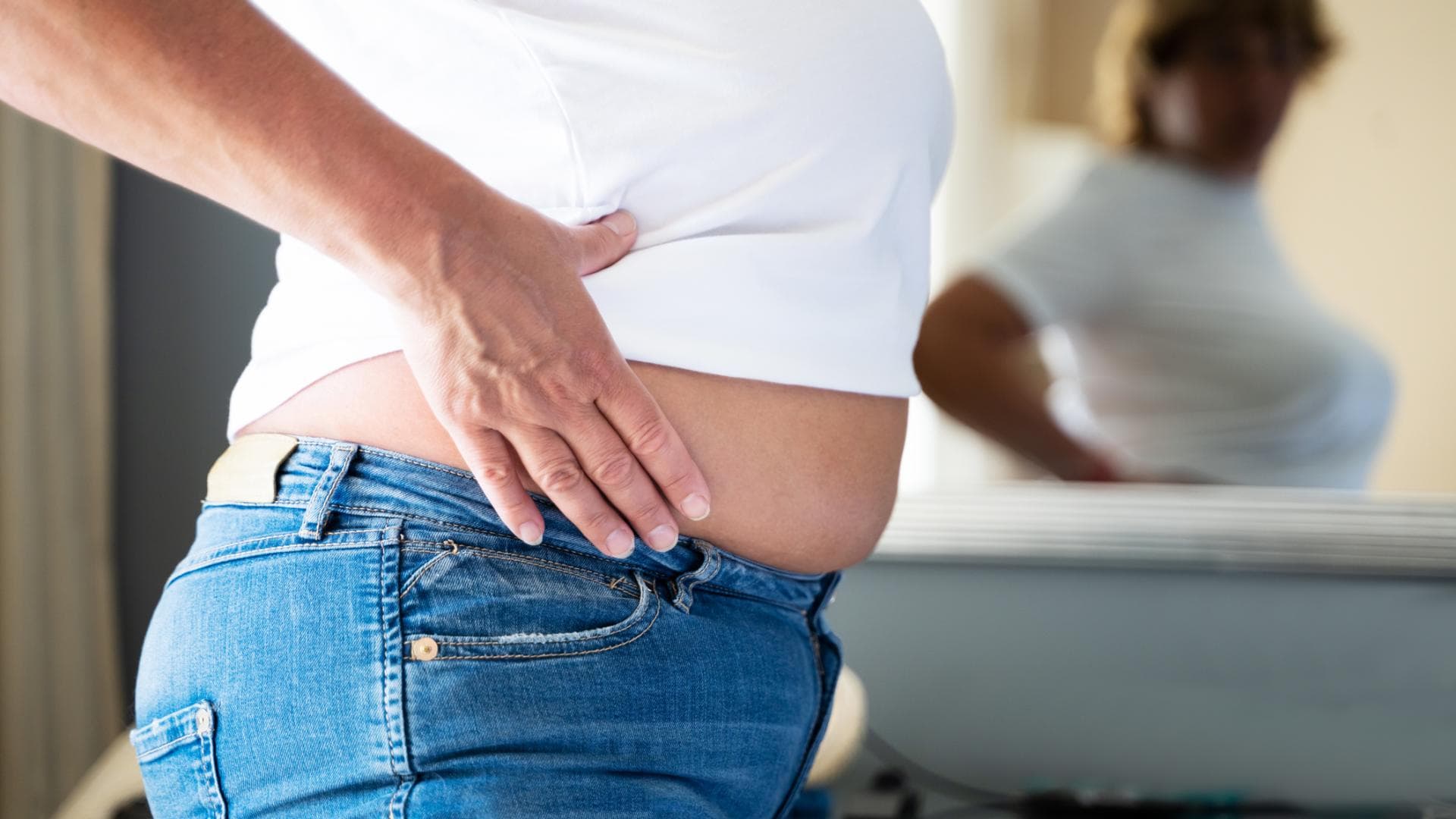 Frau guckt sich ihren Bauch im Spiegel an