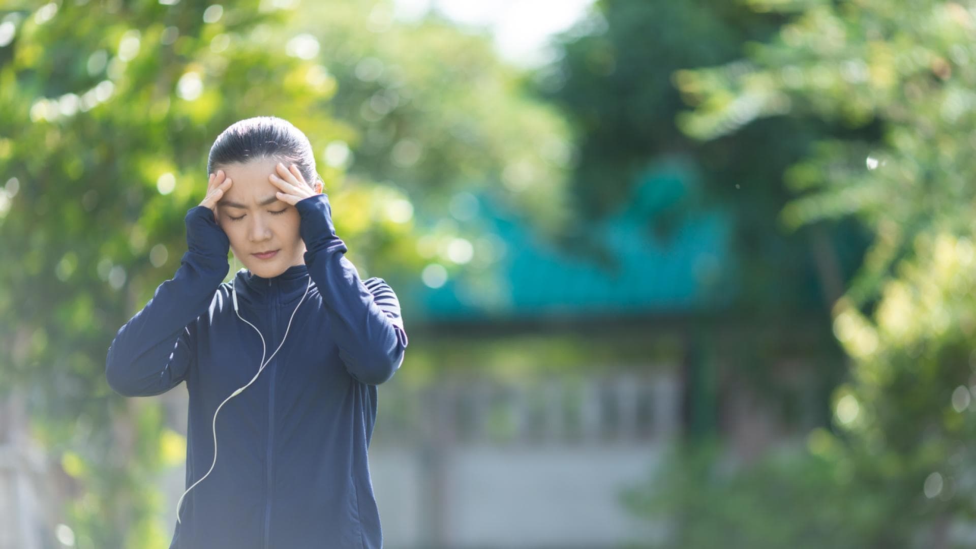 Joggerin mit Erkältung fasst sich an schmerzenden Kopf