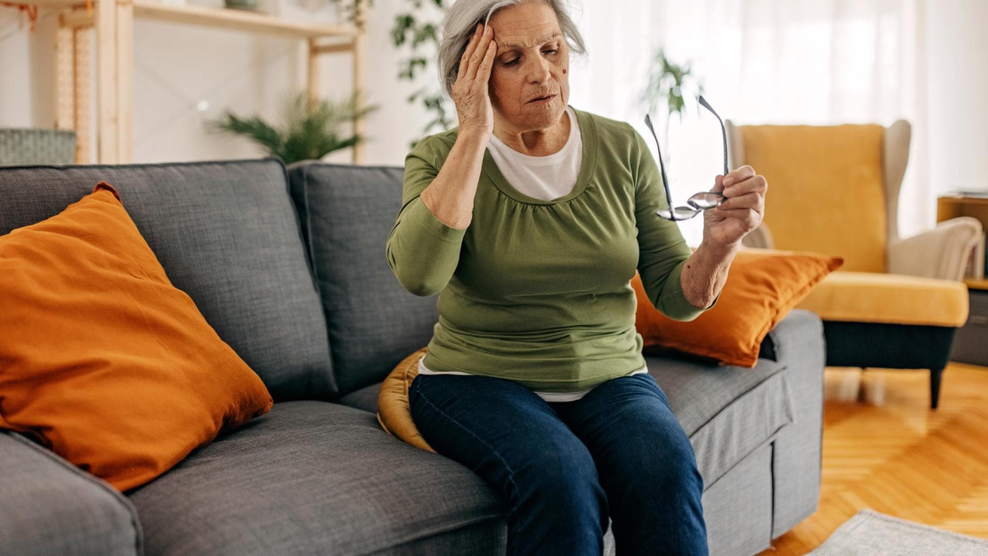 Alte Frau auf der Couch fasst sich wegen Schwindel an den Kopf