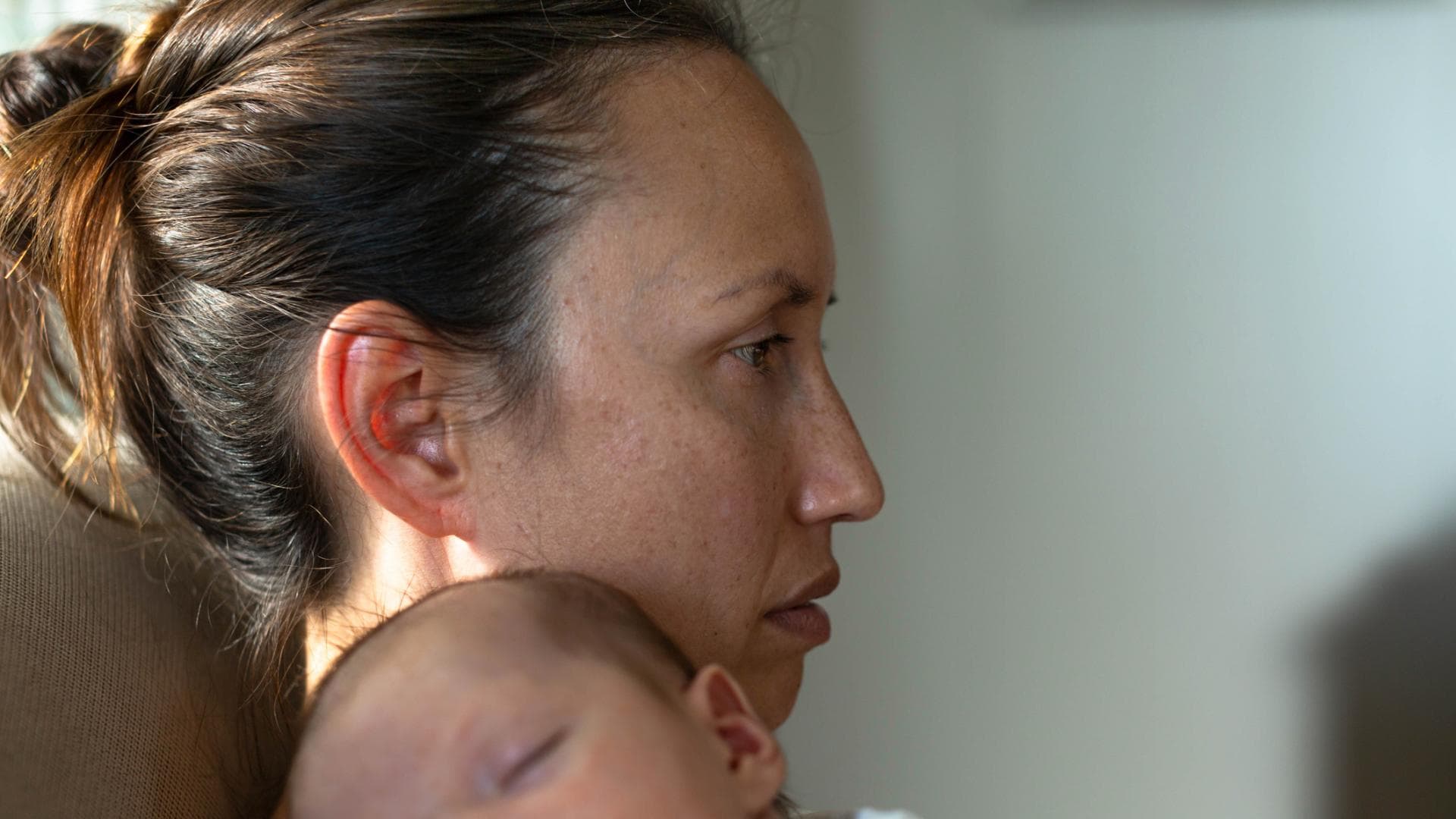 Frau mit Wochenbettdepression und Baby auf dem Arm starrt ins Leere