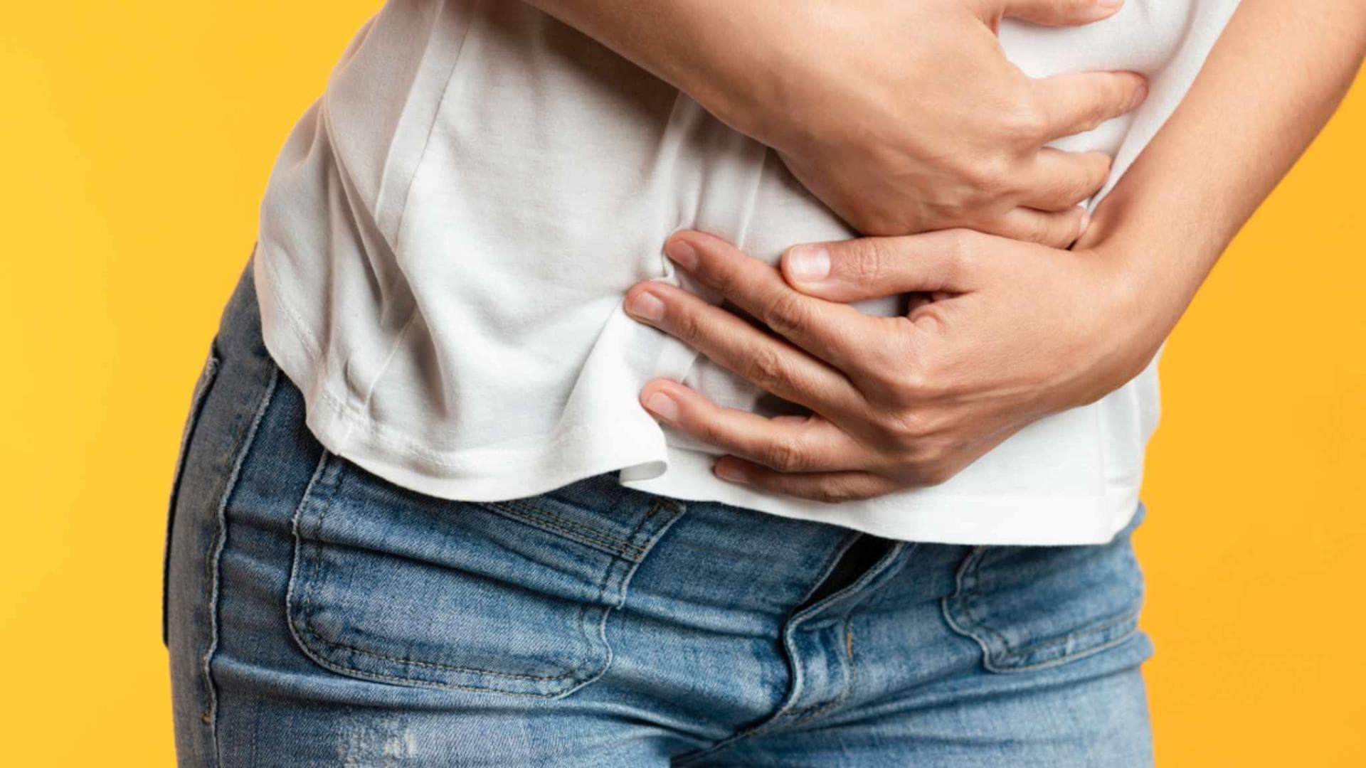 Frau vor gelbem Hintergrund hält sich schmerzenden Bauch