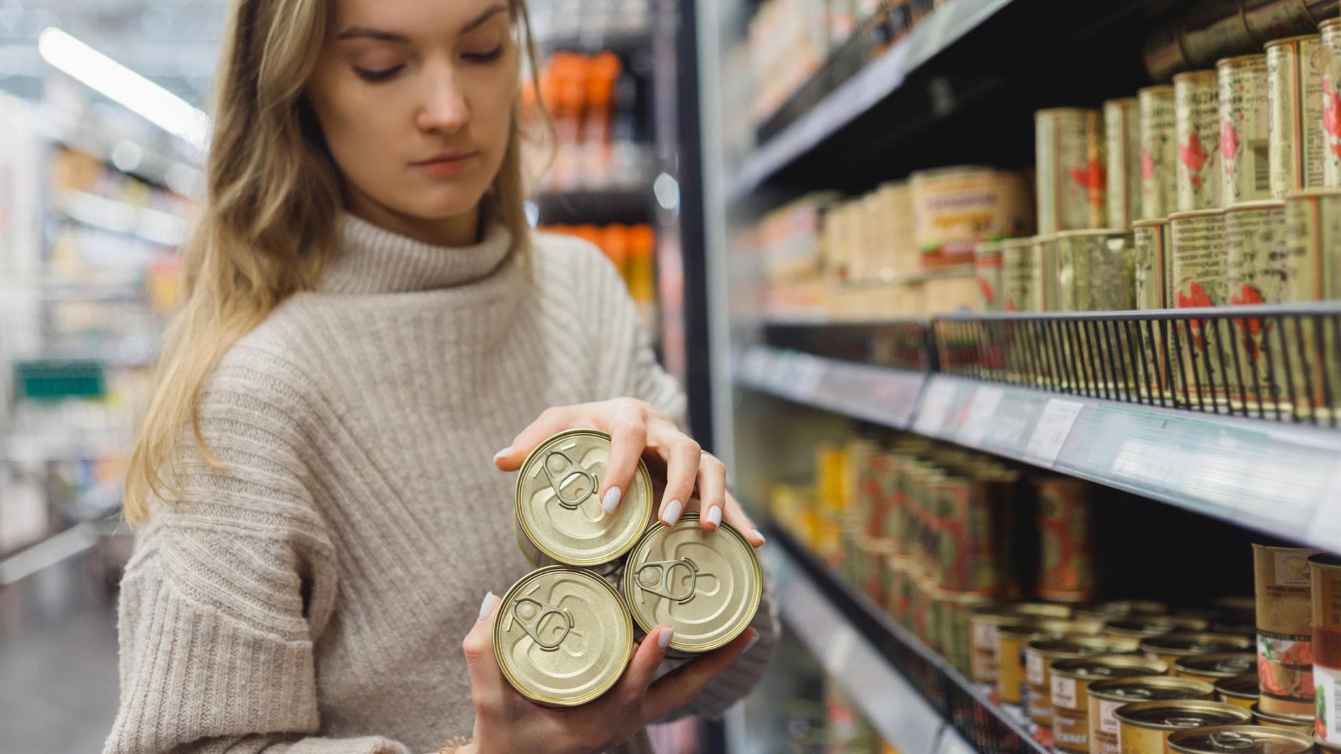 Frau nimmt Konserven aus Supermarktregal