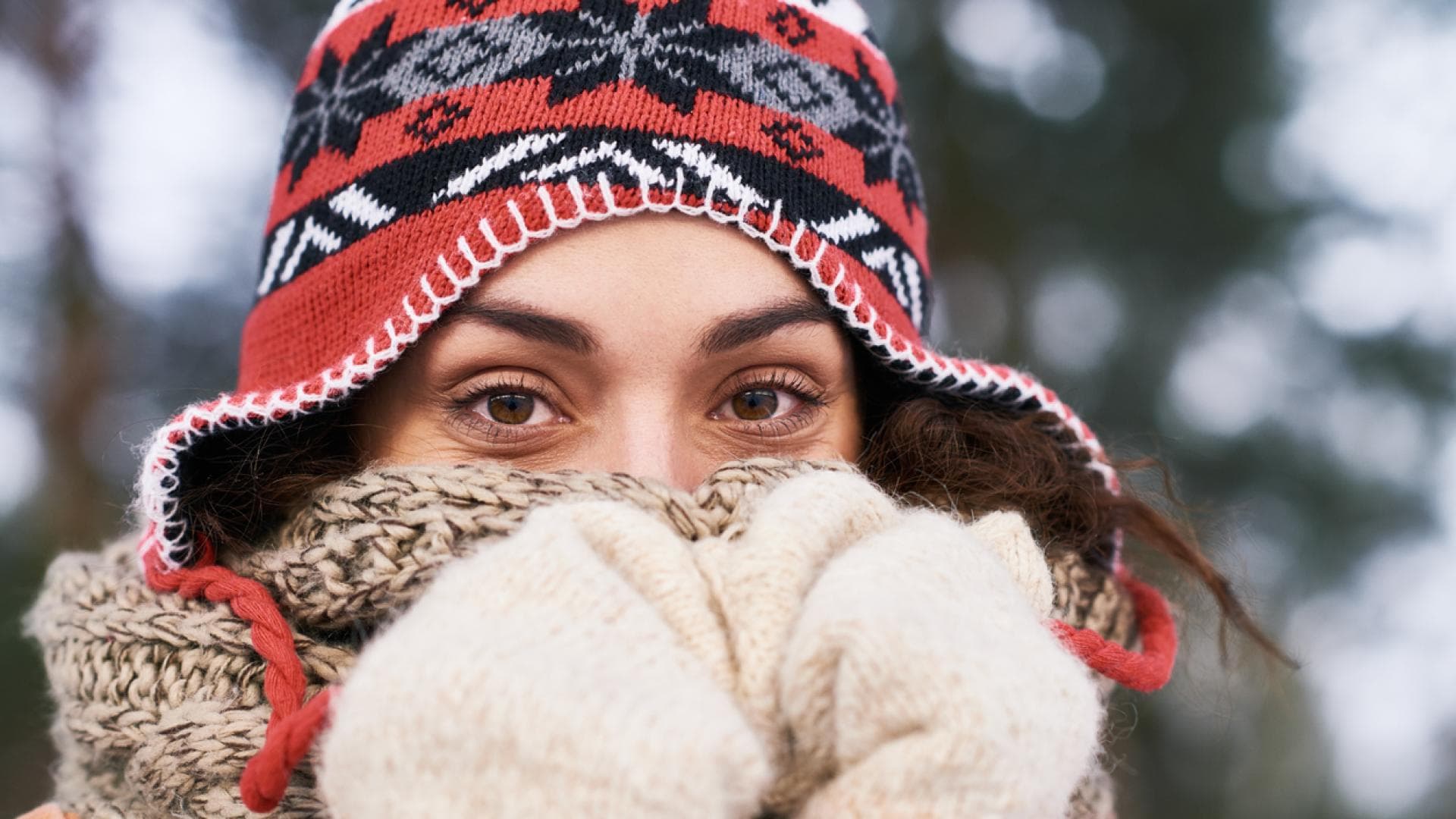 Frau mit Schlappmütze wärmt Nase im Winter unter dickem Schal
