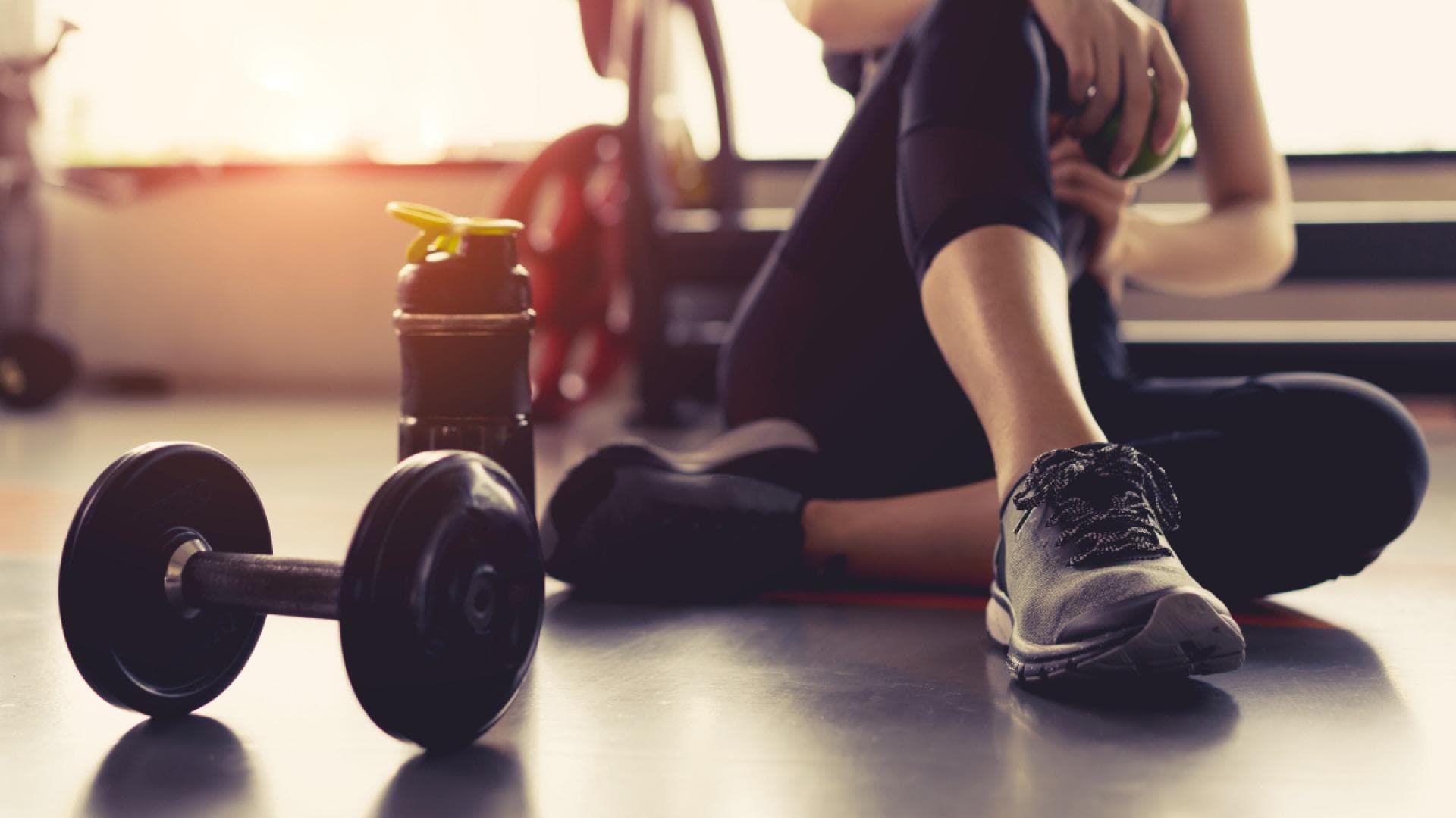 Frau sitzt erschöpft im Fitnessstudio