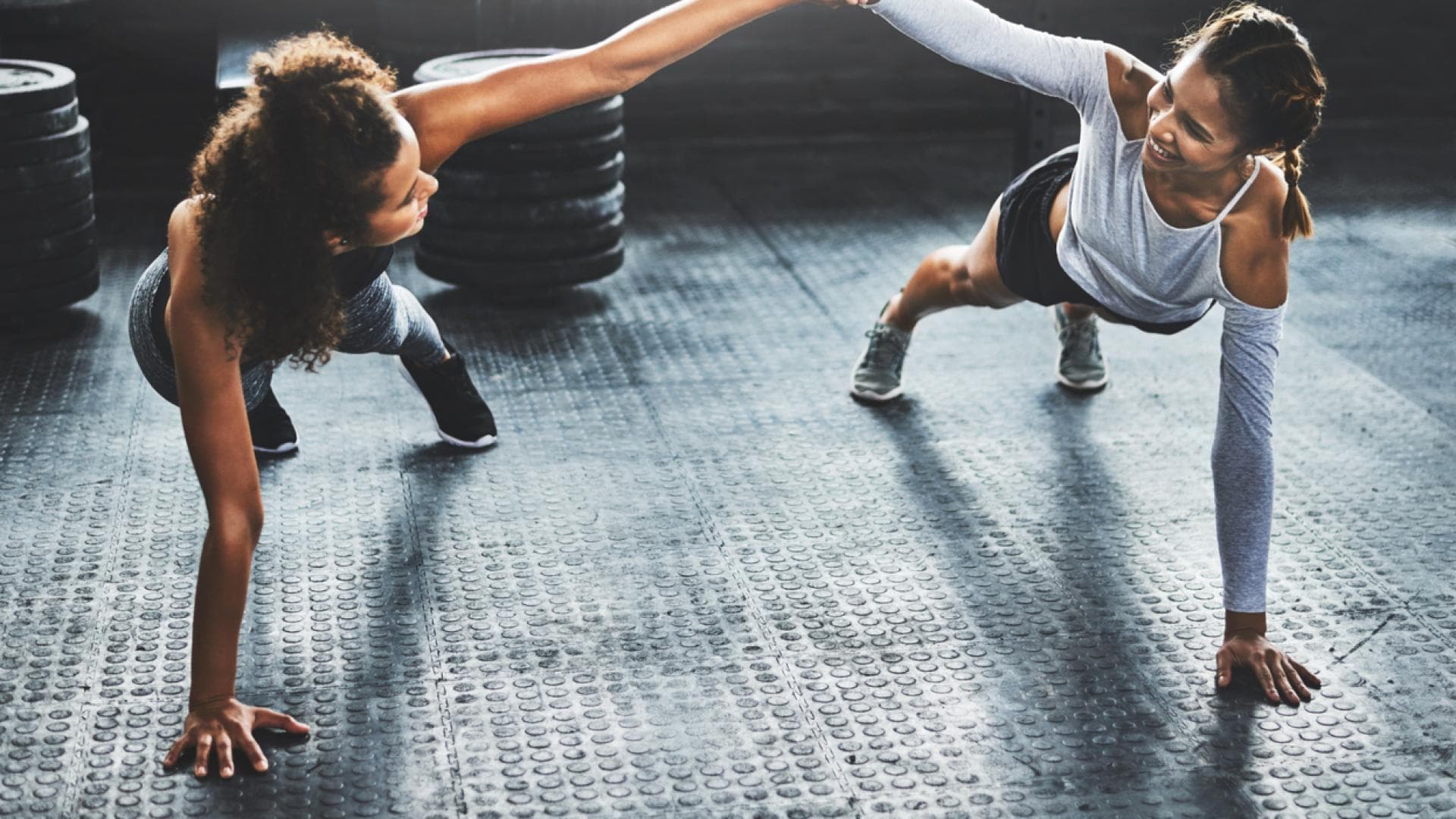 Die Partner-Plank spornt an und macht Spaß zwei Fitnessfreundinnen machen Plank zusammen und klatschen ab