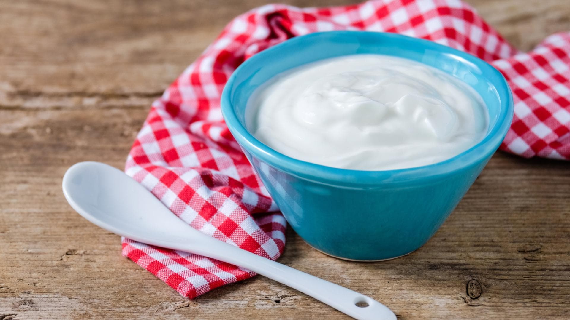Joghurt in Schüssel auf kariertem Tuch auf Tisch