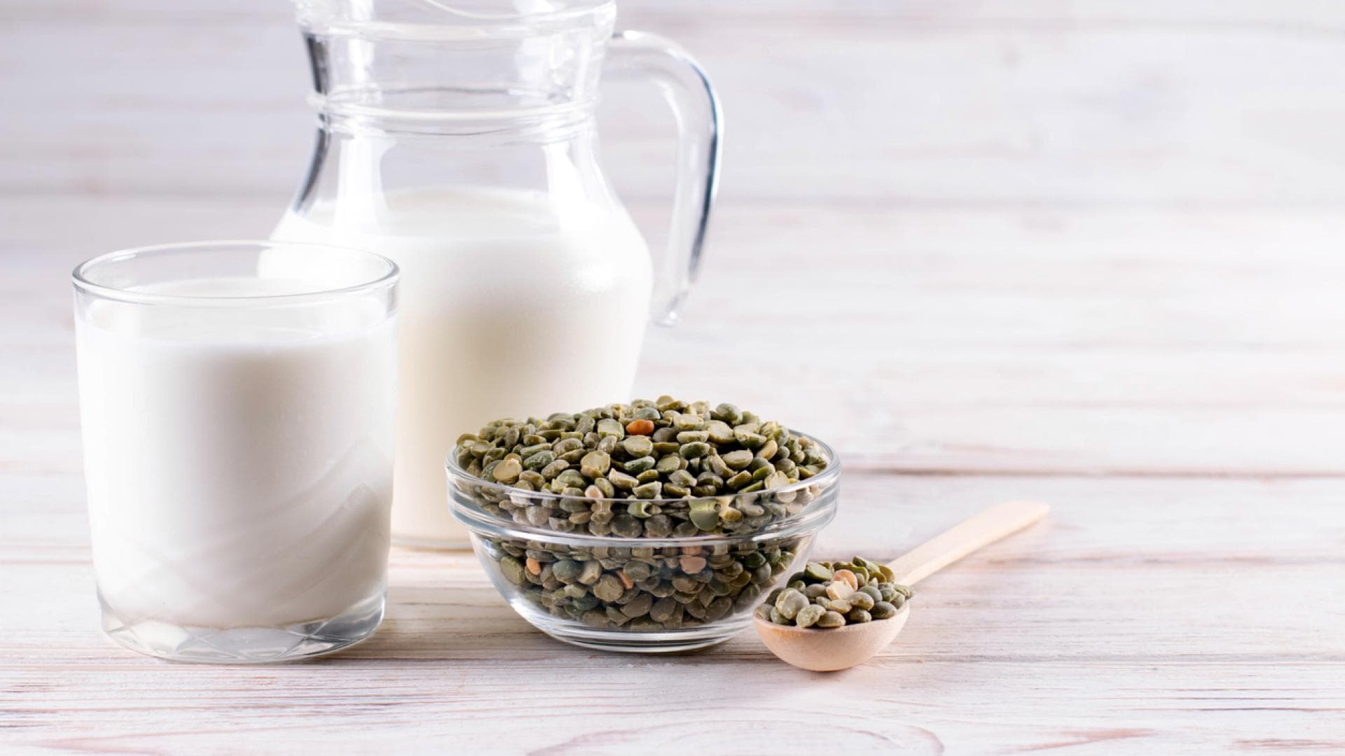 Milchglas und Karaffe mit trocknen, grünen Erbsen davor