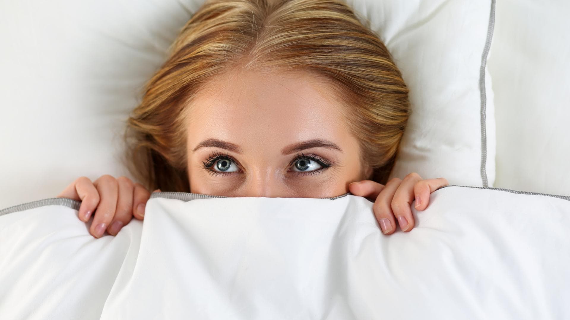 Frau liegt im Bett und verdeckt ihren Mund
