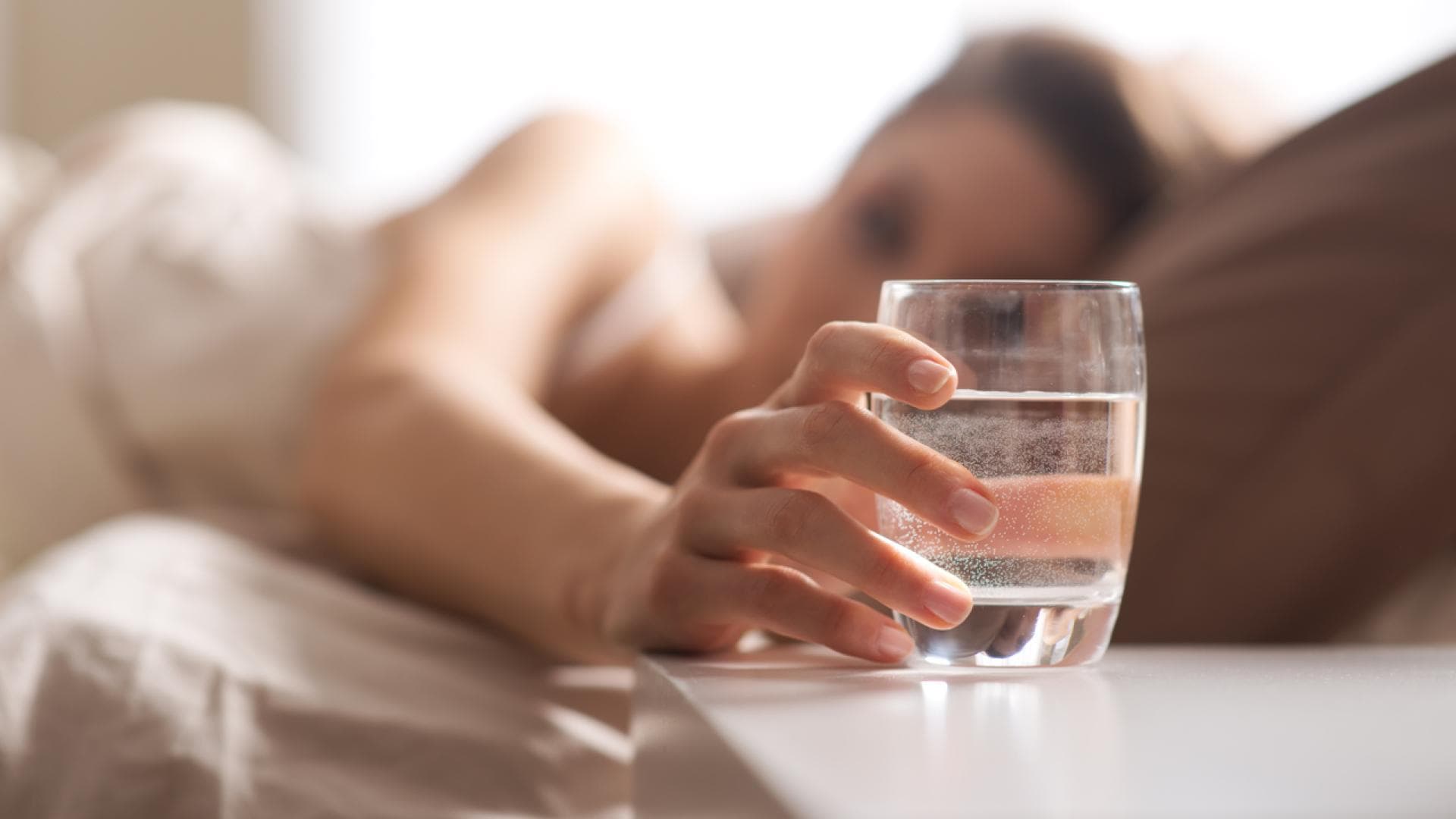 Frau trinkt Wasser im Bett