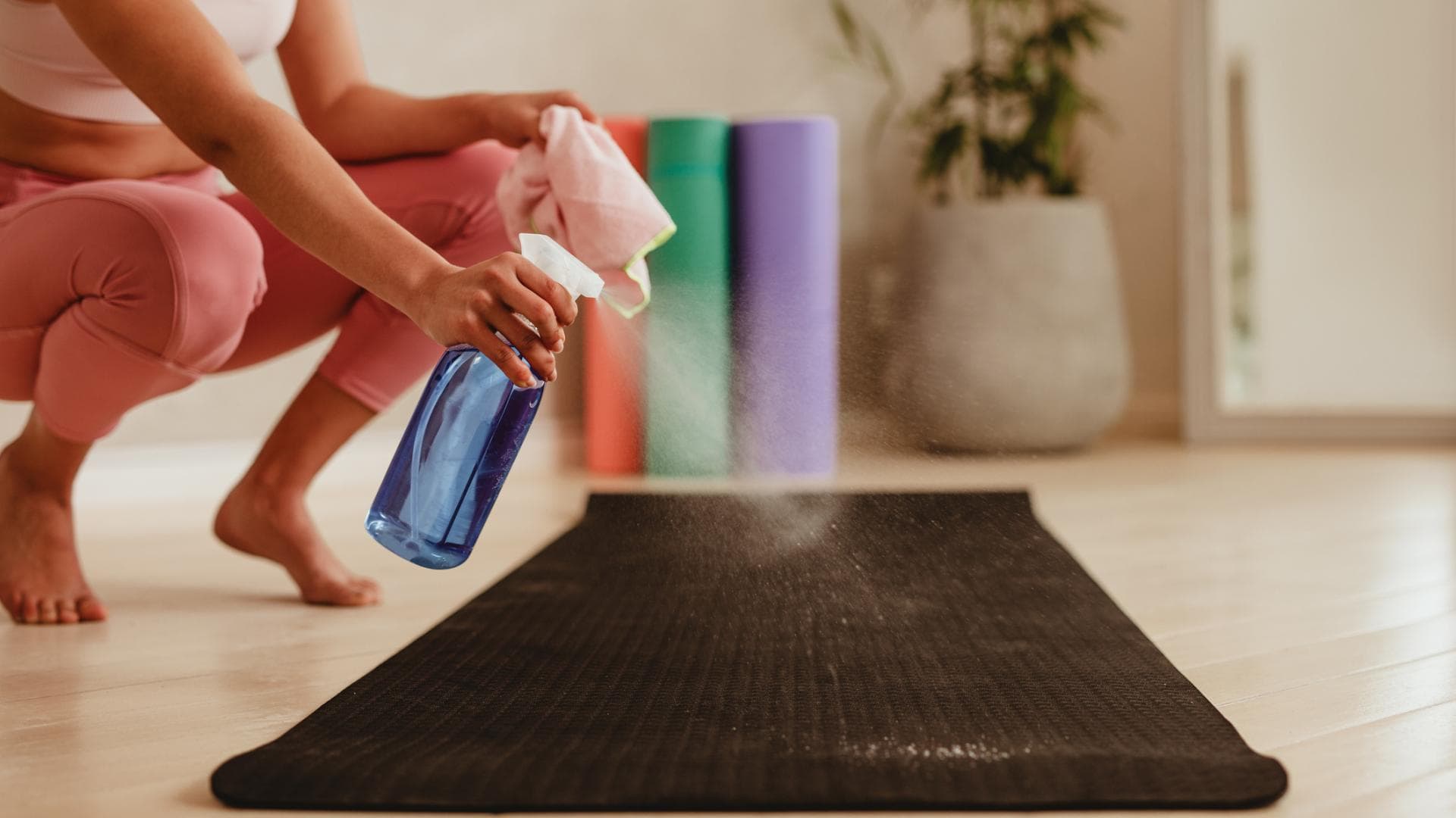 Frau Reinigung Übungsmatte mit Desinfektionsspray in Fitness-Studio