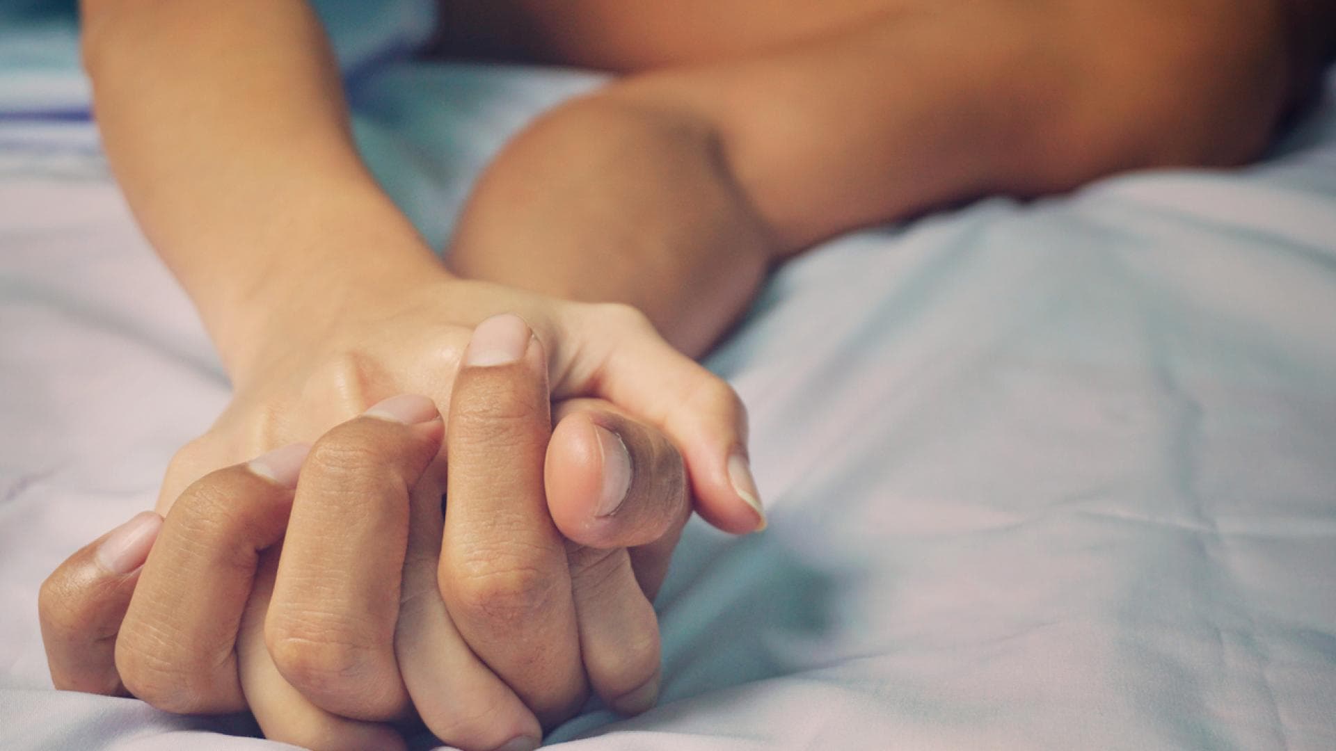 Zwei ineinander verwobene Hände im Bett