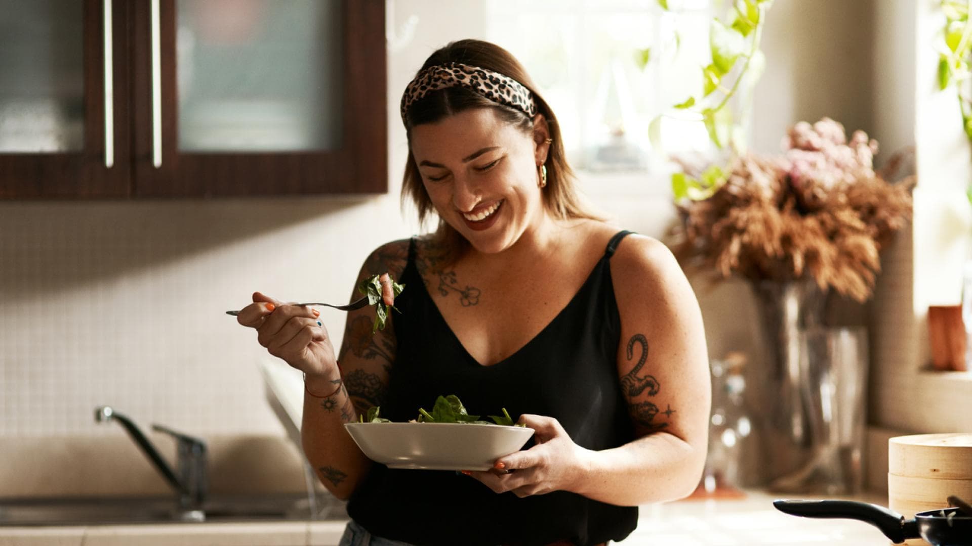 glückliche Frau mit Tattoos isst Salat