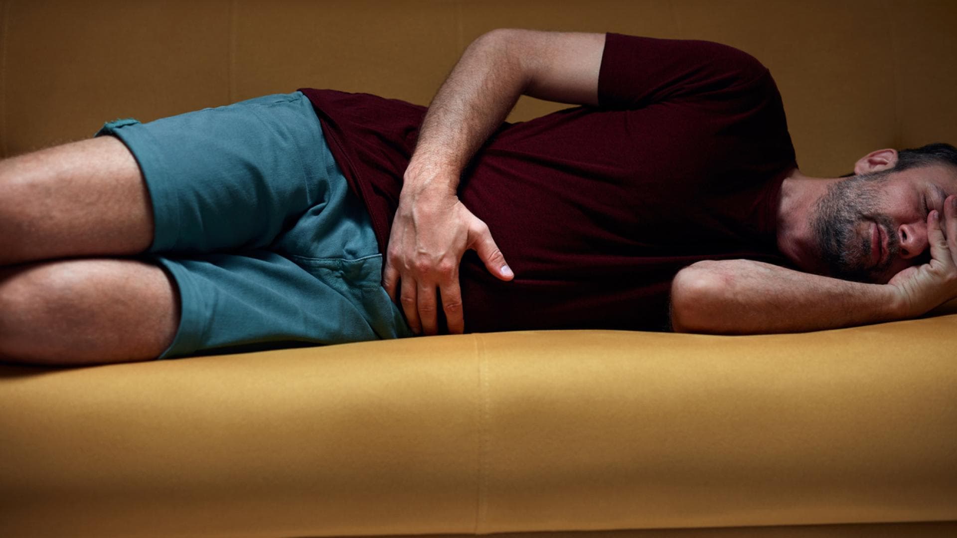 Mann mit Bauchschmerzen liegt auf gelber Couch