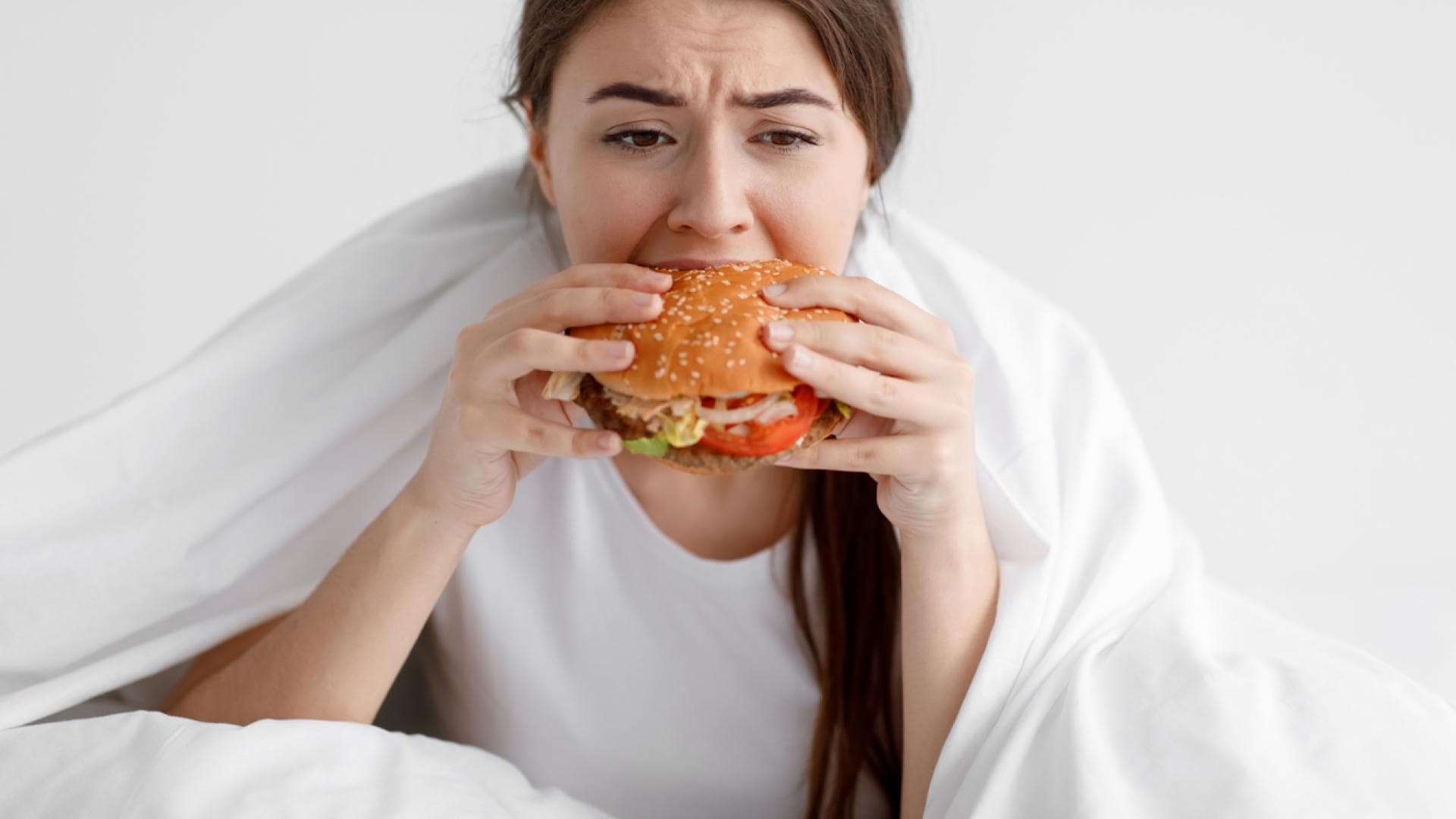 Frau isst im Bett einen Burger