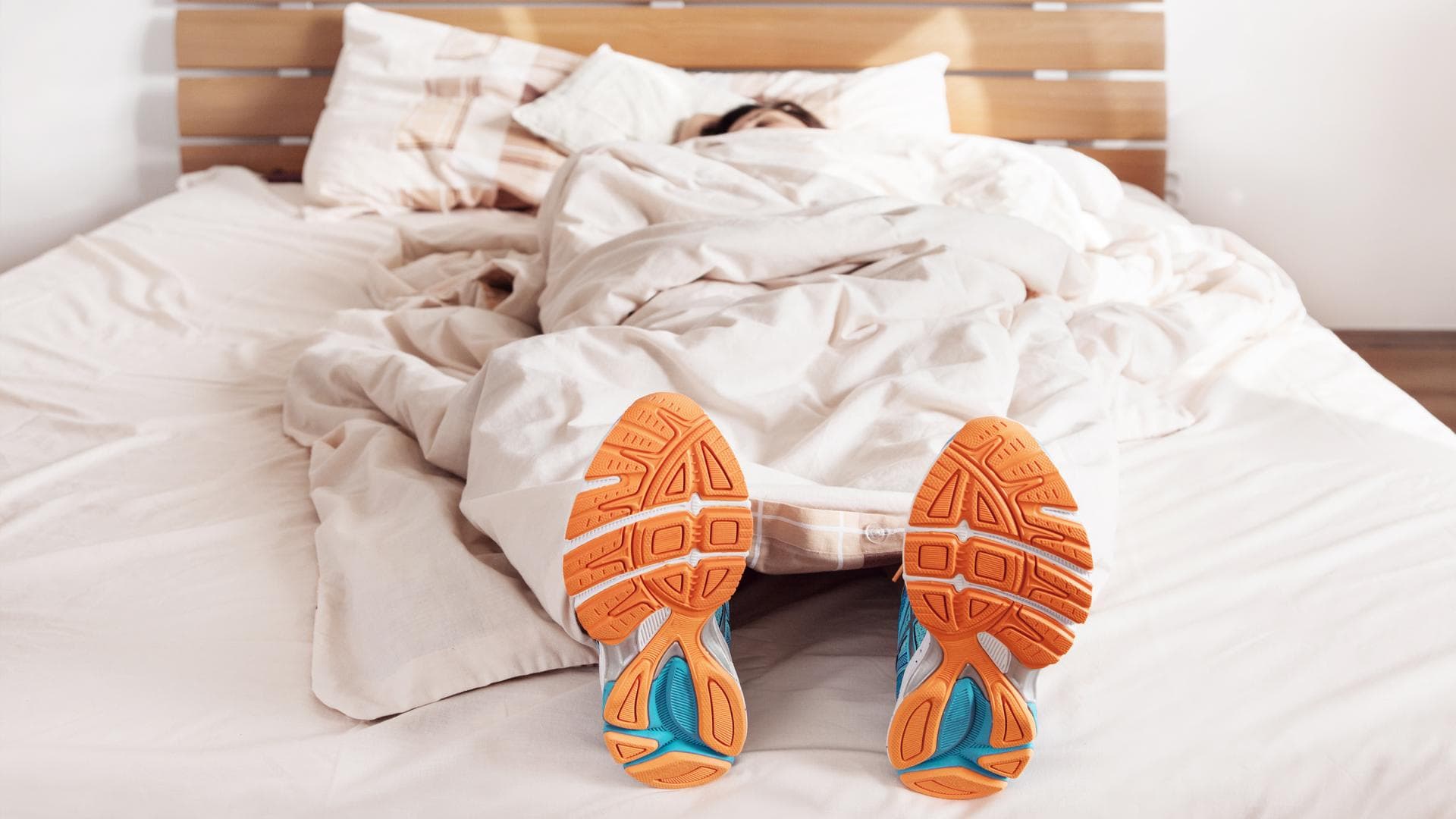 Sportler liegt mit Sportschuhen im Bett