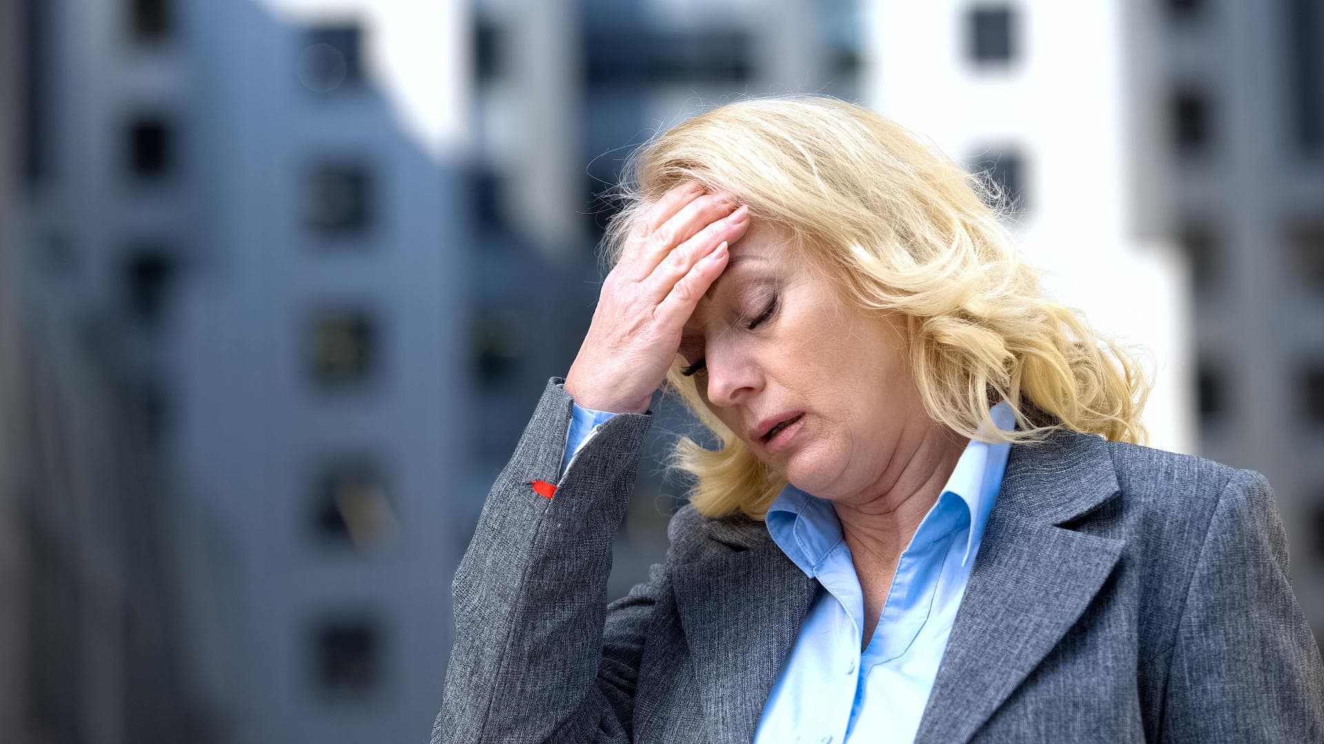 Blonde Frau mit Burnout fasst sich erschöpft an den Kopf