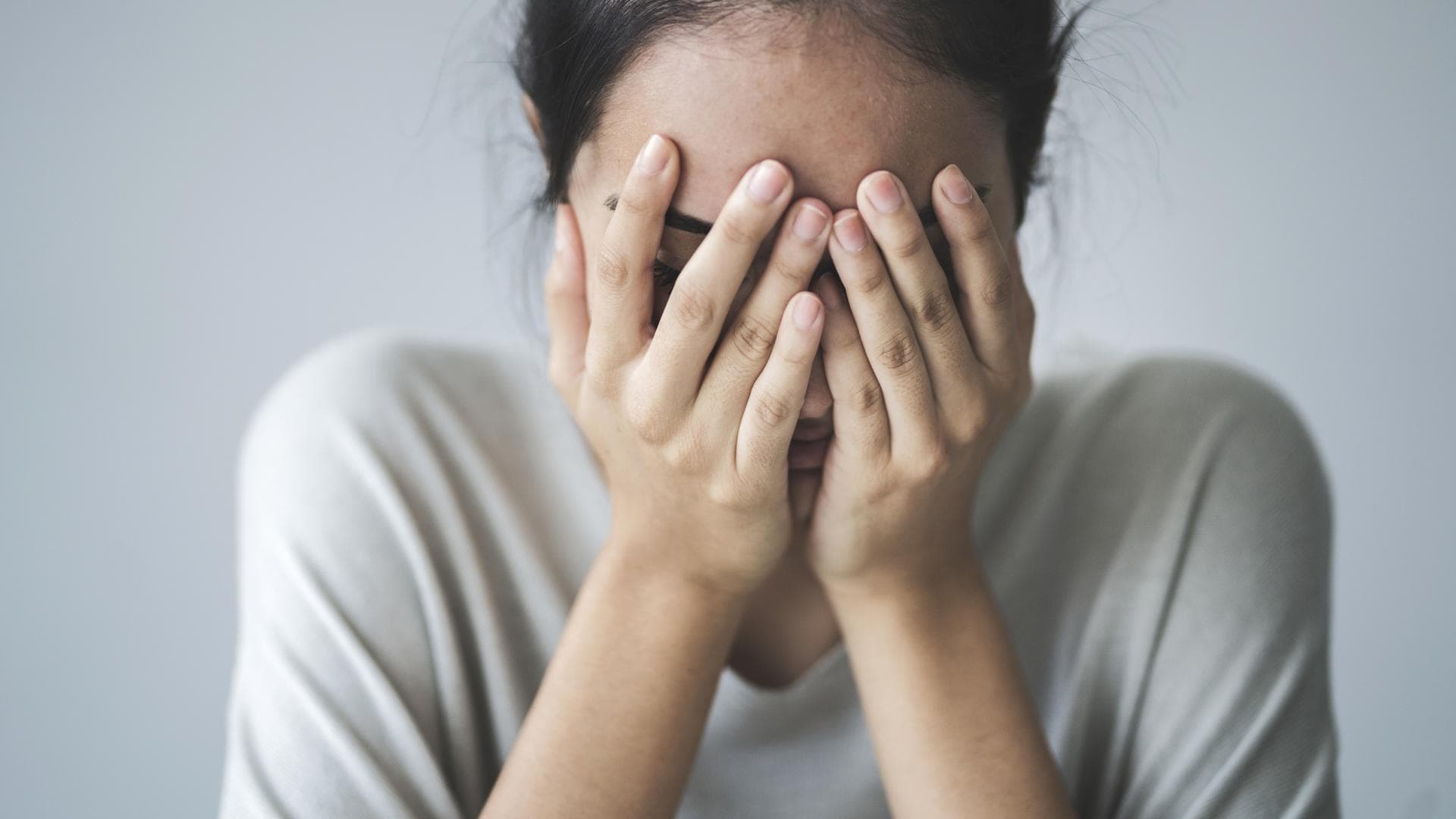 Junge Frau mit Moebius Syndrom schlägt Hände vors Gesicht