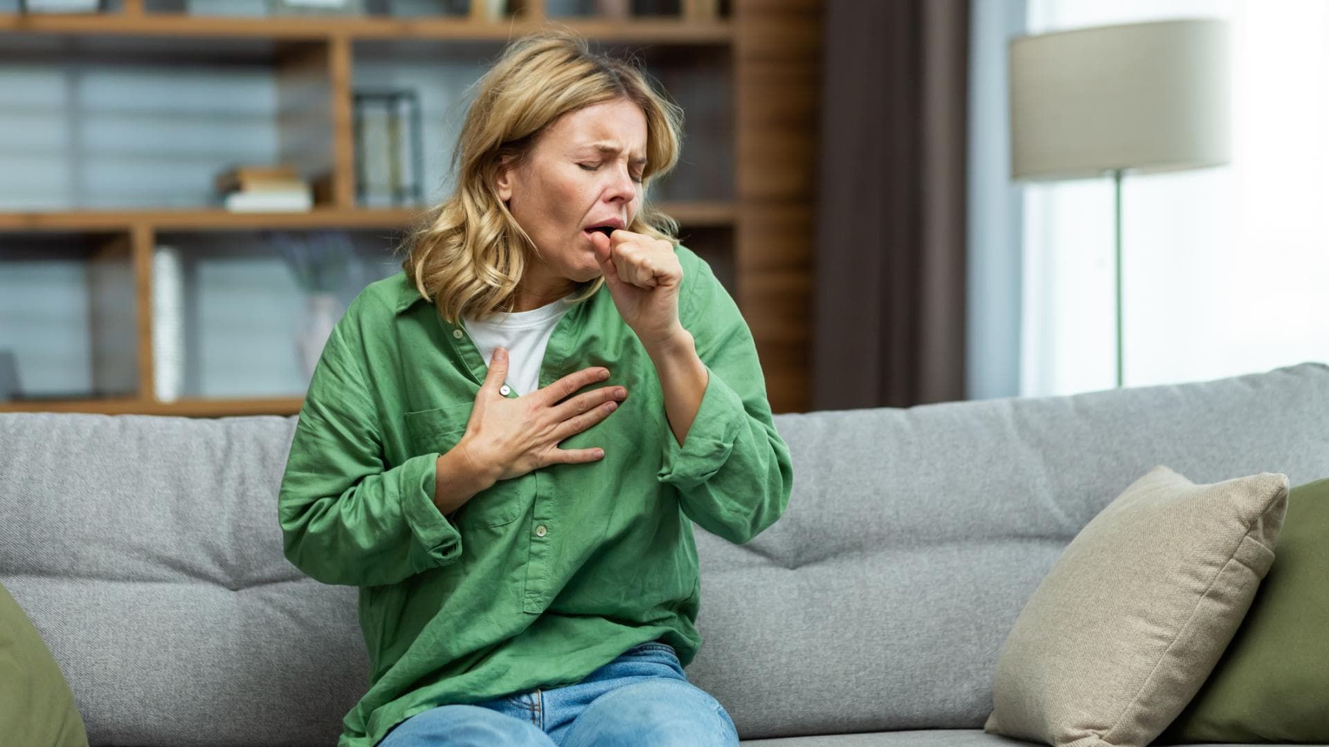 Frau sitzt auf dem Sofa und hustet Frau sitzt auf dem Sofa und hustet