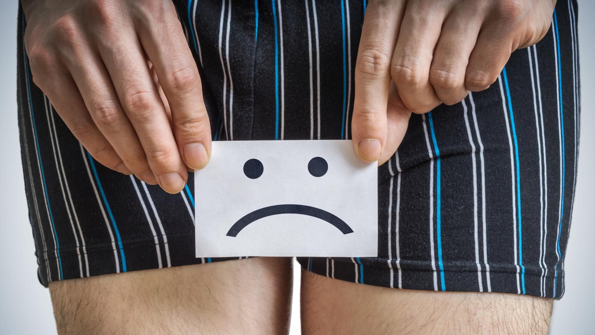 Mann hält ein Schild mit traurigem Smiley vor seinen Unterleib