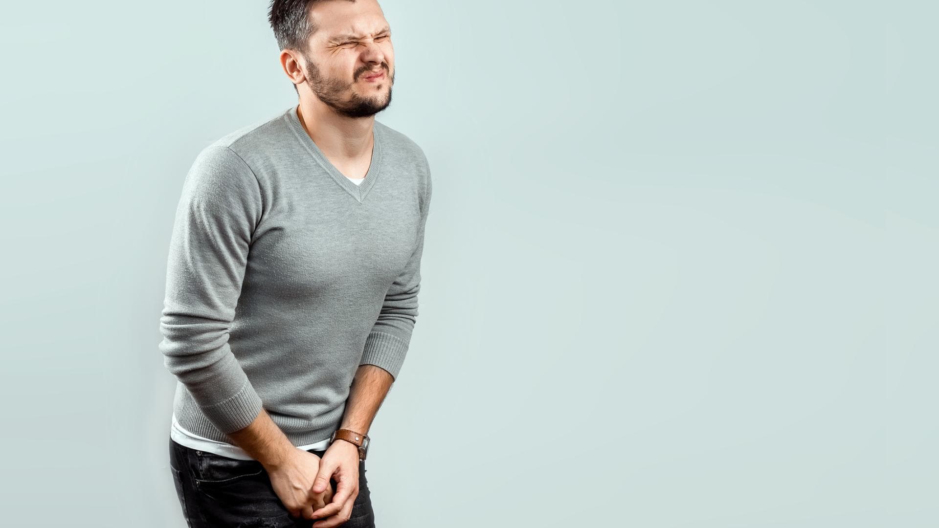Mann fasst sich mit schmerzverzerrtem Gesicht zwischen die Beine Mann fasst sich mit schmerzverzerrtem Gesicht zwischen die Beine