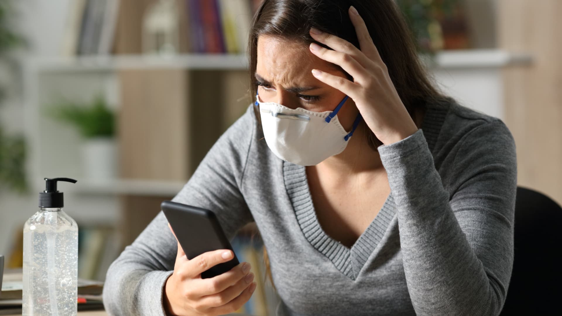 Frau trägt eine Maske und guckt besorgt auf ihr Handy