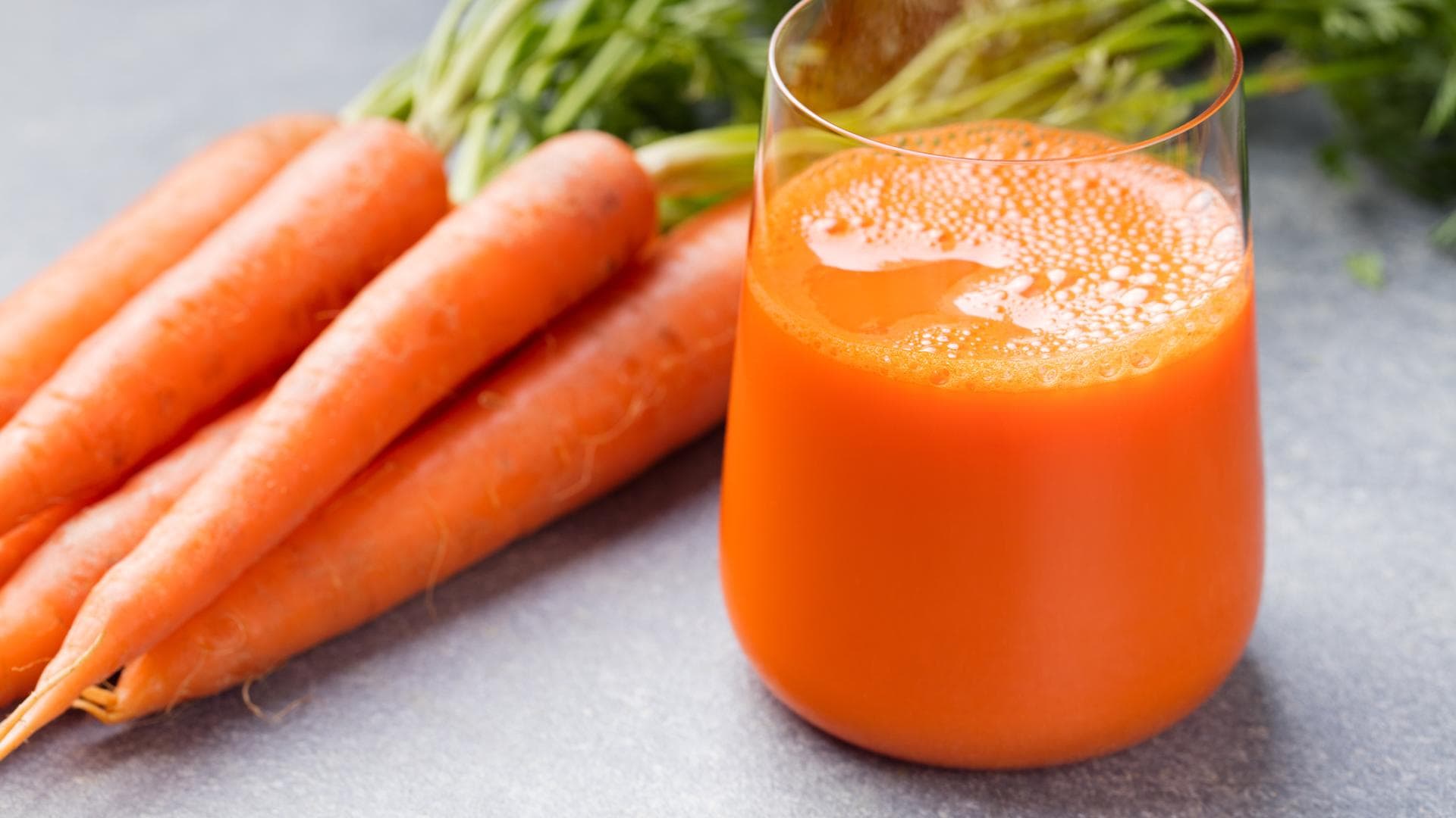 Karottensaft ist richtig gesund Ein Glas frisch gepresster Karottensaft mit einem Bündel Karotten daneben