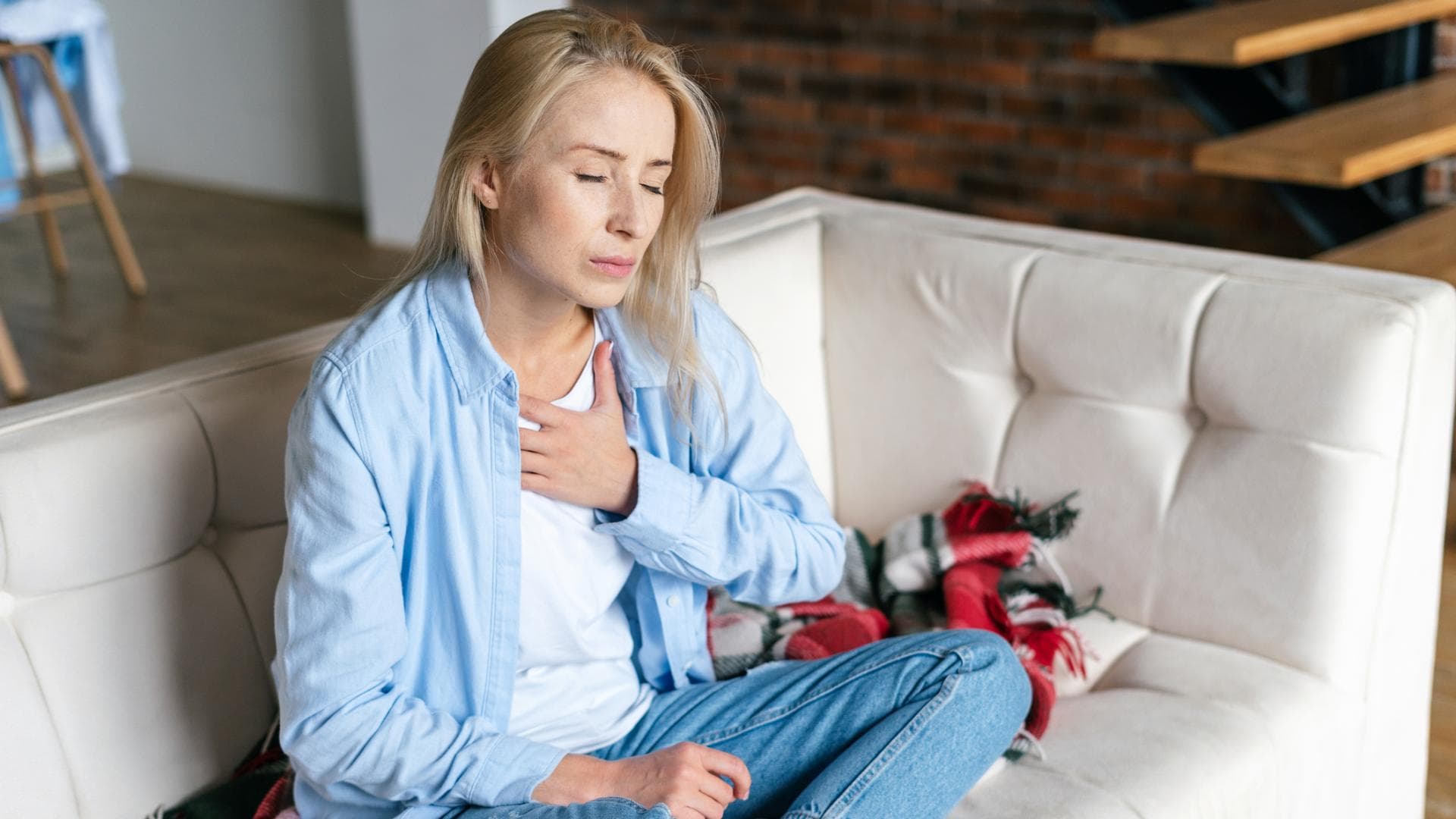 Frau sitz auf Sofa und fasst sich an die Brust