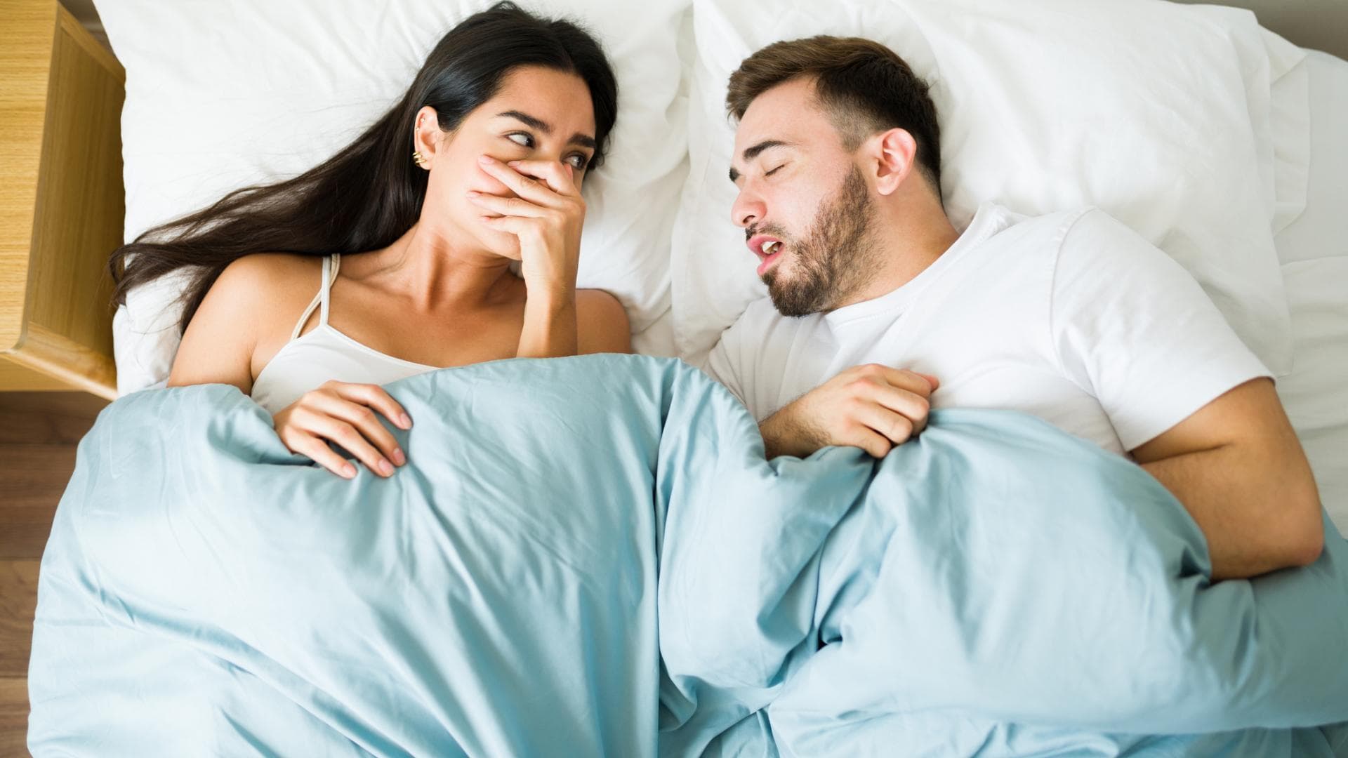 Frau liegt neben ihrem Freund im Bett und hält sich die Hand vor den Mund Frau liegt neben ihrem Freund im Bett und hält sich die Hand vor den Mund