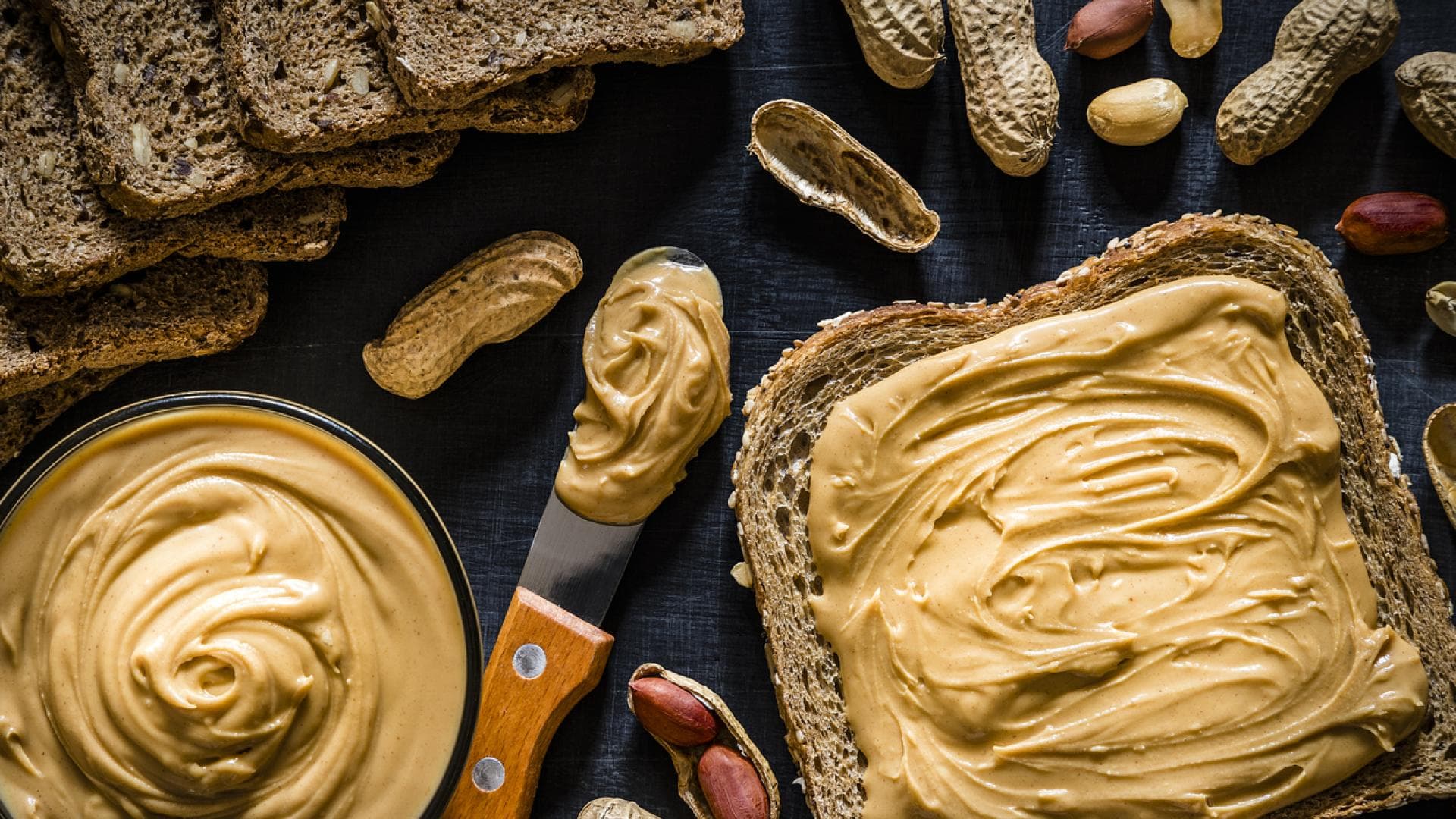 Nussbutter: Gesund oder ungesund? Cremige Nussbutter im Schälchen und auf einem Vollkorntoast