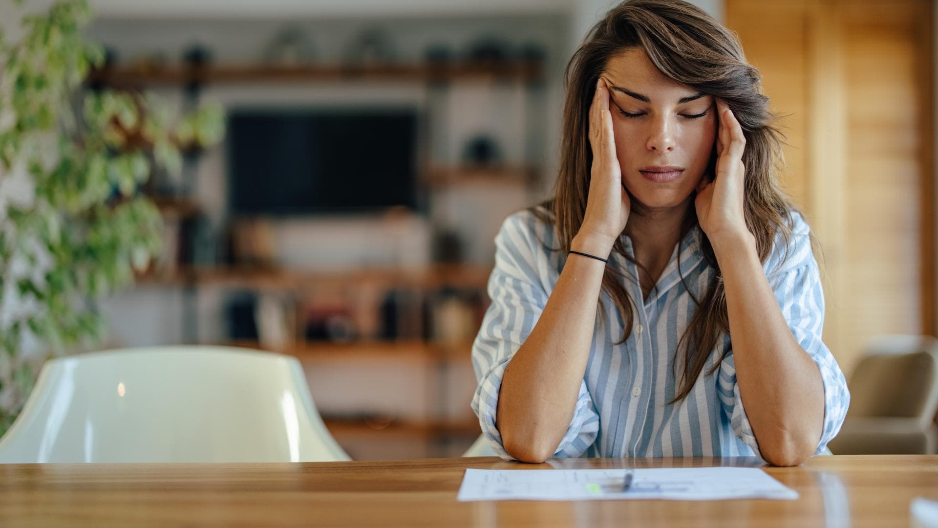 People Pleasing kann sehr viel Stress verursachen gestresste Frau im Büro massiert sich mit geschlossenen Augen die Schläfen