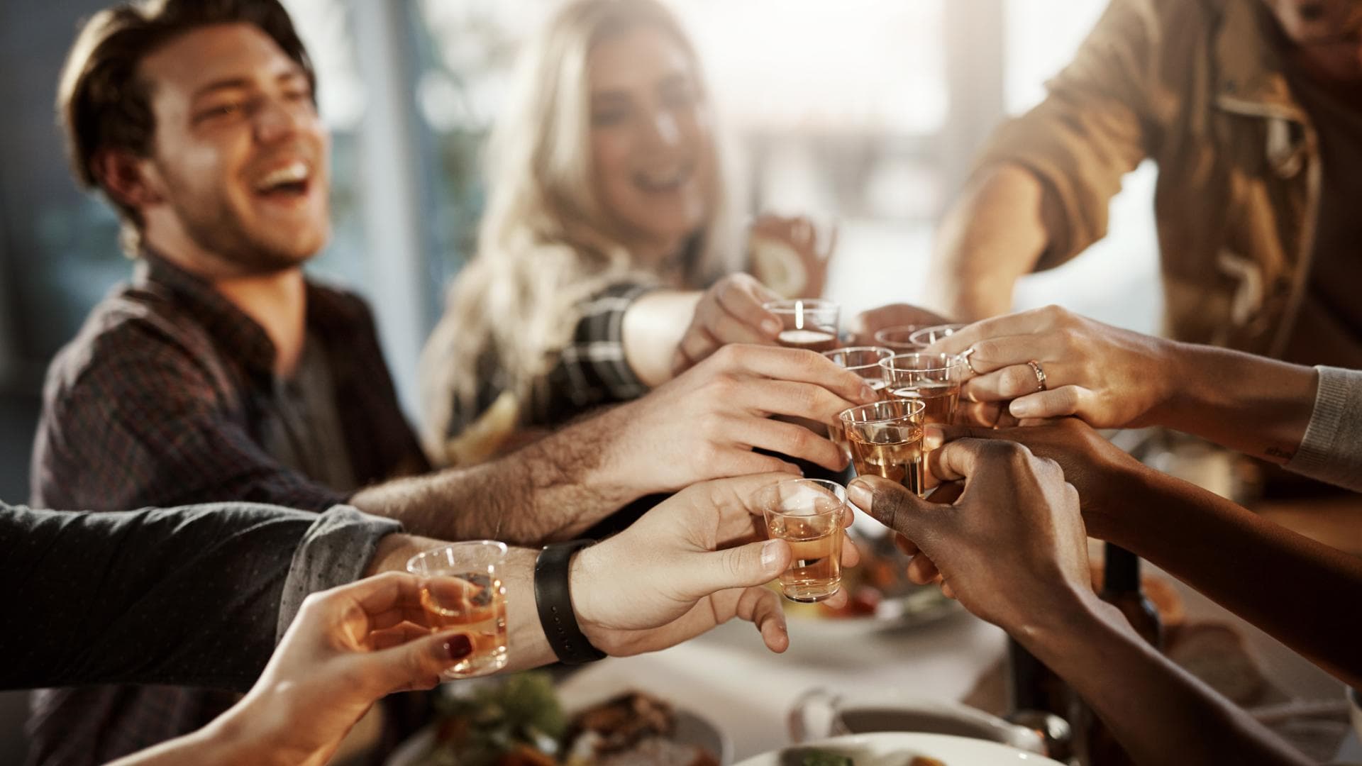 Gemischte Gruppe aus Freunden stößt mit kleinen Schnäpsen beim Essen an