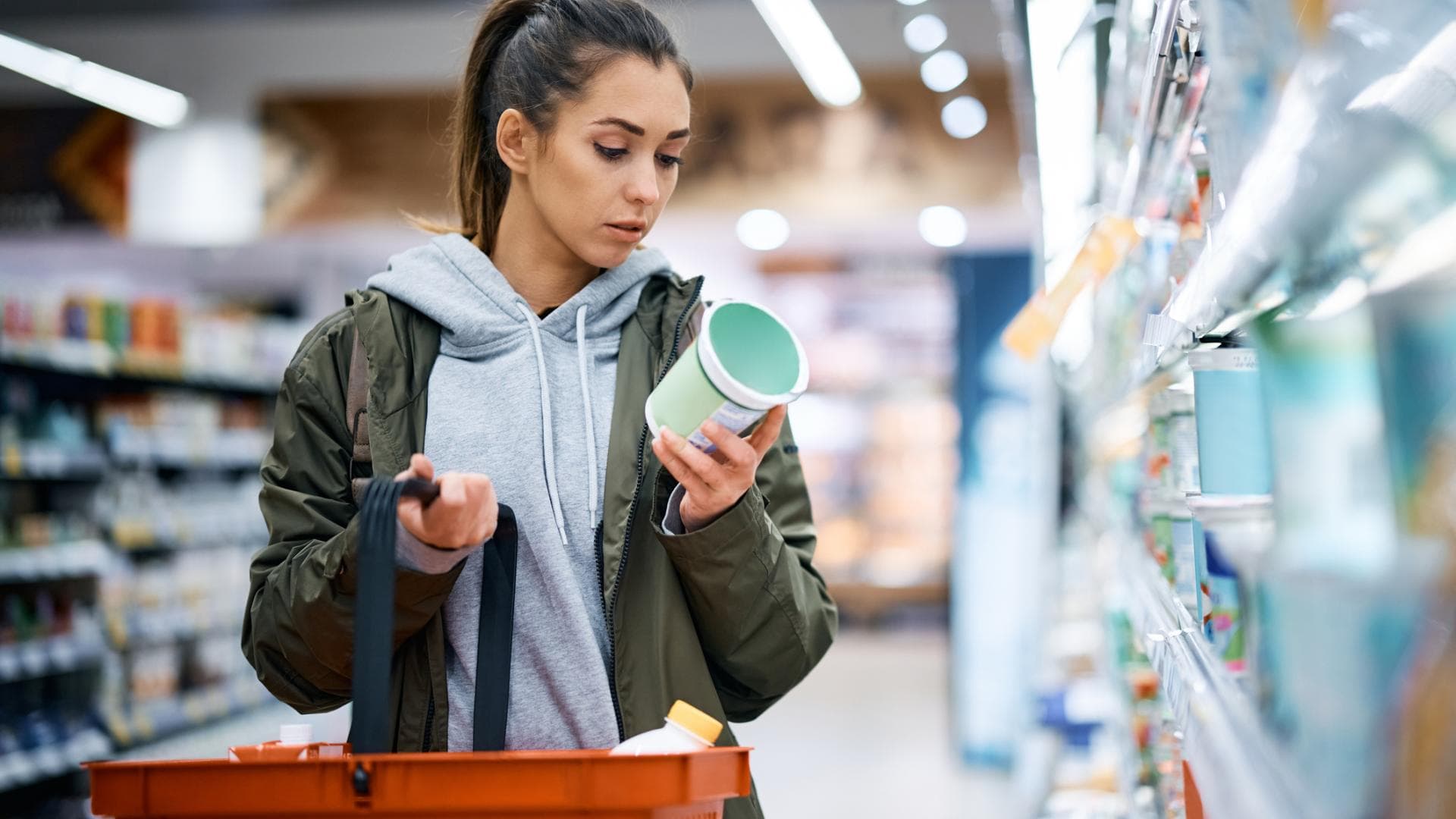 Wie stark verarbeitet sind meine Lieblingslebensmittel eigentlich wirklich? Frau im Supermarkt liest Zutatenliste eines Eiscreme-Bechers aufmerksam