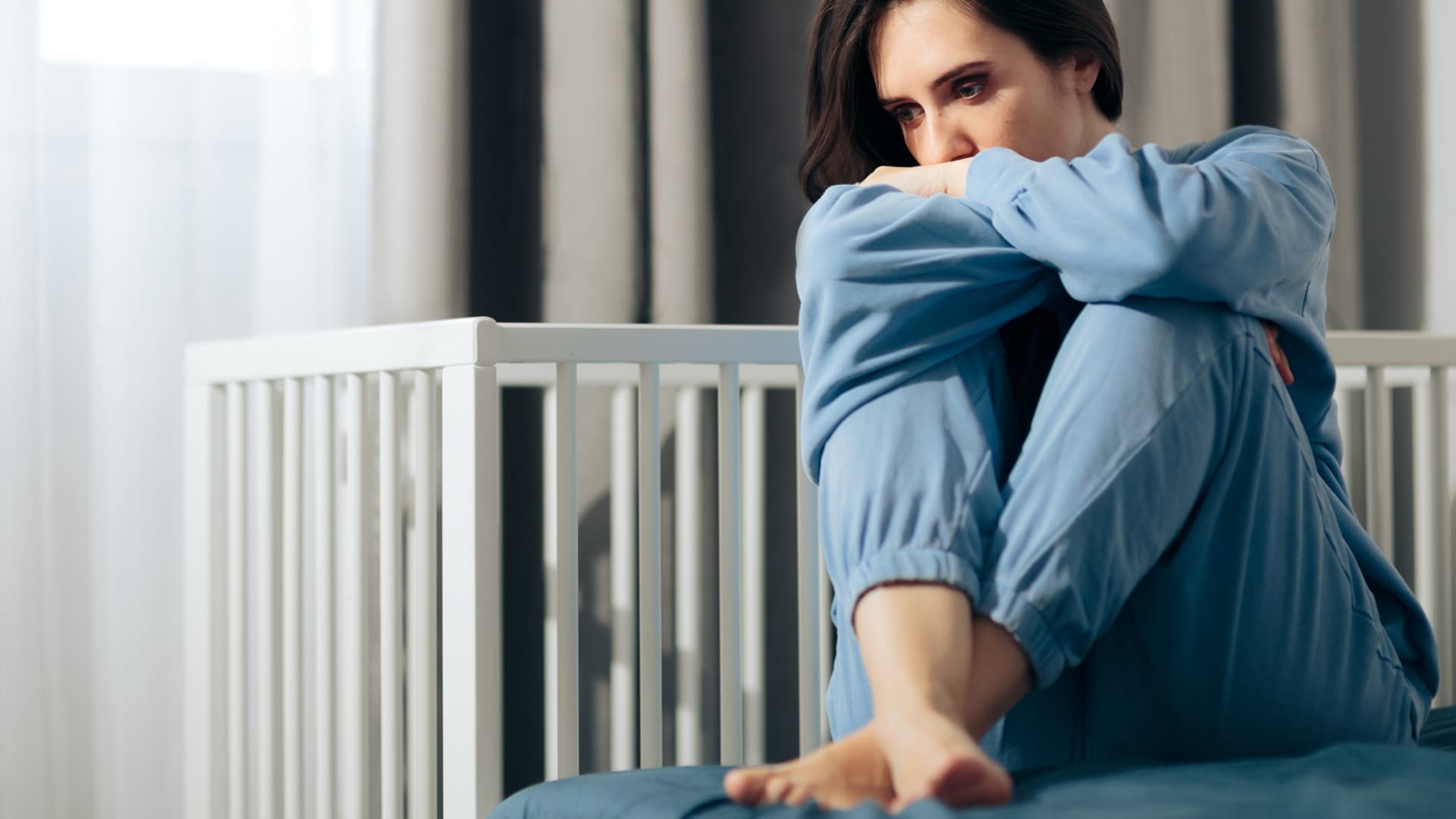 Wenn schreckliche Erinnerungen zurückbleiben, zum Beispiel der Verlust eines Kindes, spricht man von einer Traumafolgestörung. Eine traurige Frau sitzt vor einem leeren Kinderbettchen