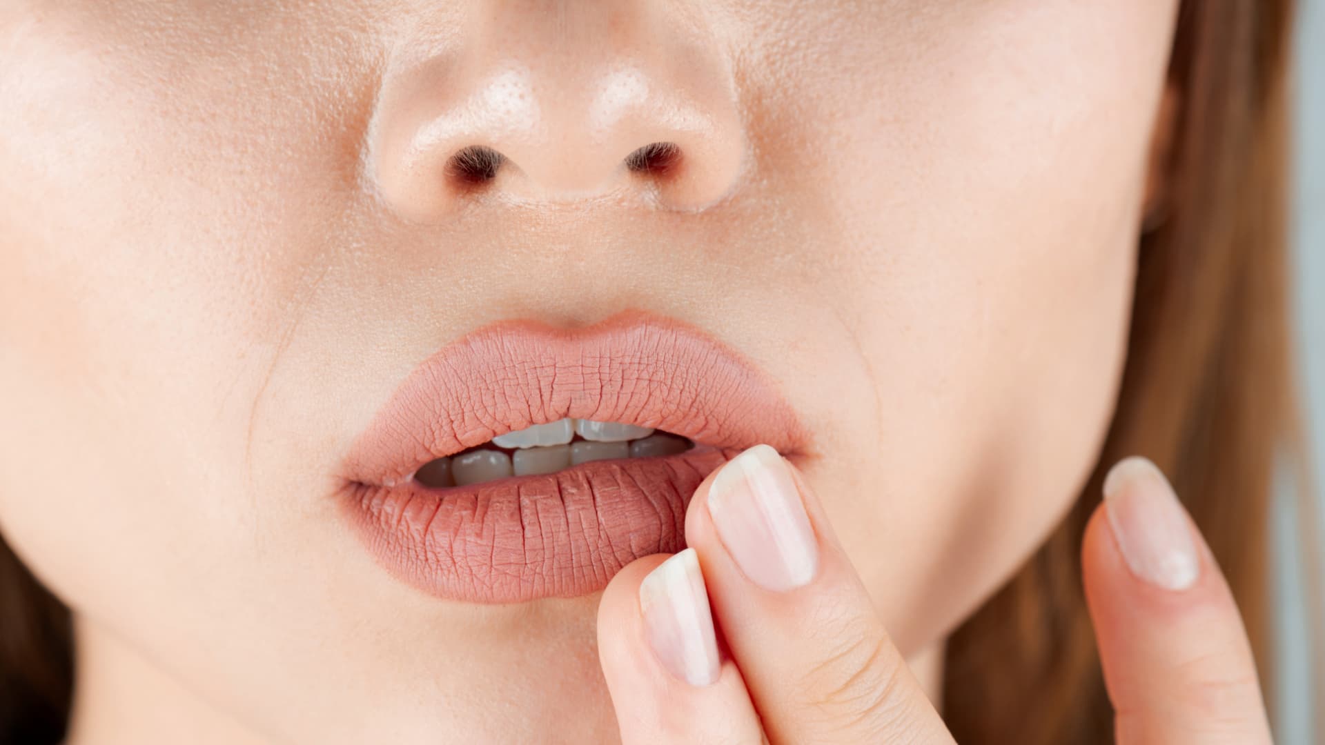 Tritt ein trockener Mund häufiger und ohne erkennbaren Grund auf, sollten Sie einen Arzt aufsuchen. Frau greift sich an die Lippen